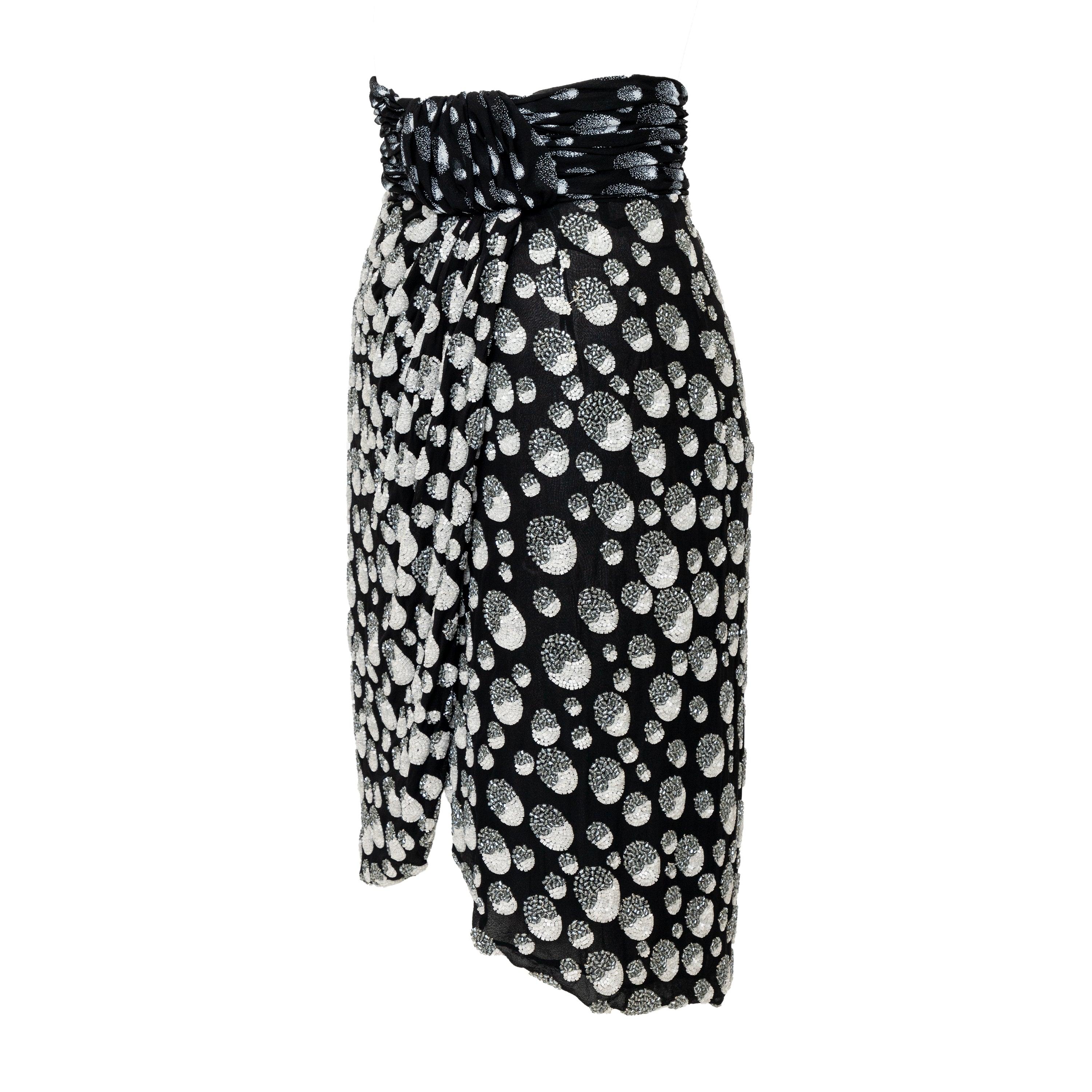 This vintage Mila Schön cocktail skirt from the 90s is a fashion staple with its unique white and grey circle pattern heavily beaded. The wrap with knot design on the front adds a touch of unique flair, while the full lining and mid-length make it
