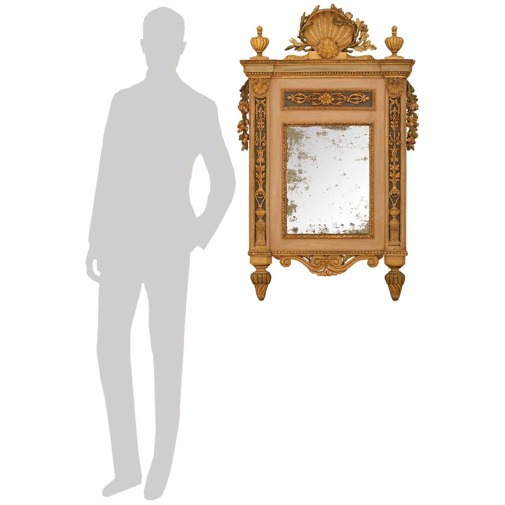 Magnifique et très décoratif miroir milanais d'époque Louis XVI en bois patiné et bois doré. Cet élégant miroir est centré en bas par une réserve en bois doré à volutes, flanquée de chaque côté de fleurons cannelés en spirale, et au-dessous d'un