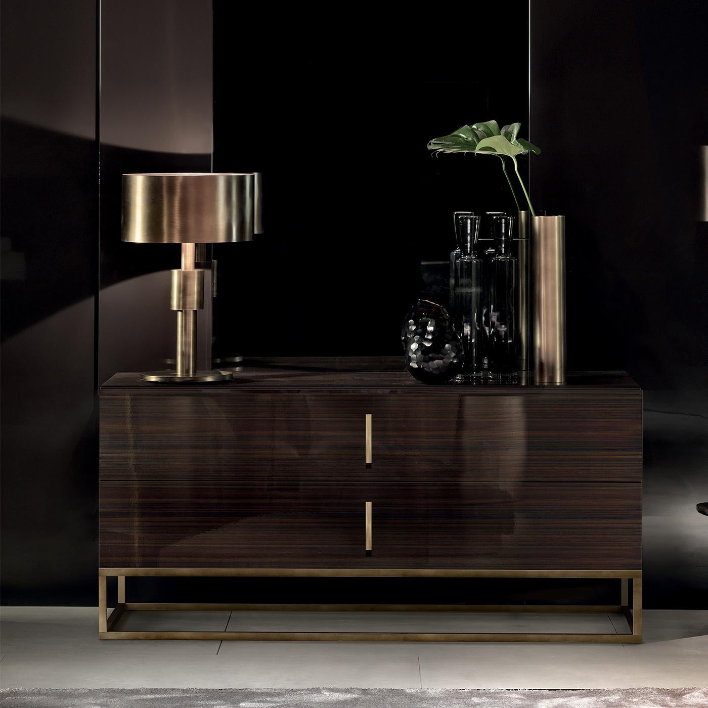 Raised on a burnished brass tubular base, the sleek silhouette and dark hued palette of this remarkable dresser merge style with functionality. Two sliding drawers with burnished brass handles open to reveal a fabric interior. Made of plywood with