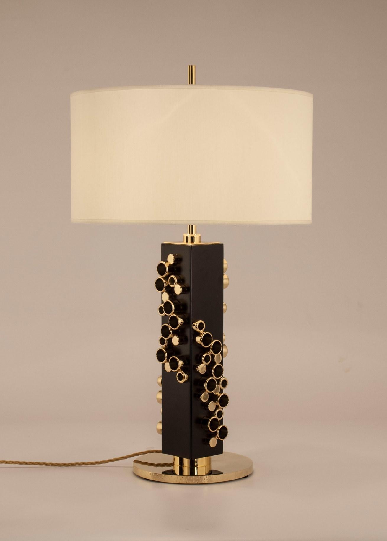Lamp with decorated cast brass base, black lacquered wooden frame decorated with precious cylindrical brass details with gold bath. Circular lampshade in ivory colored shantung.
