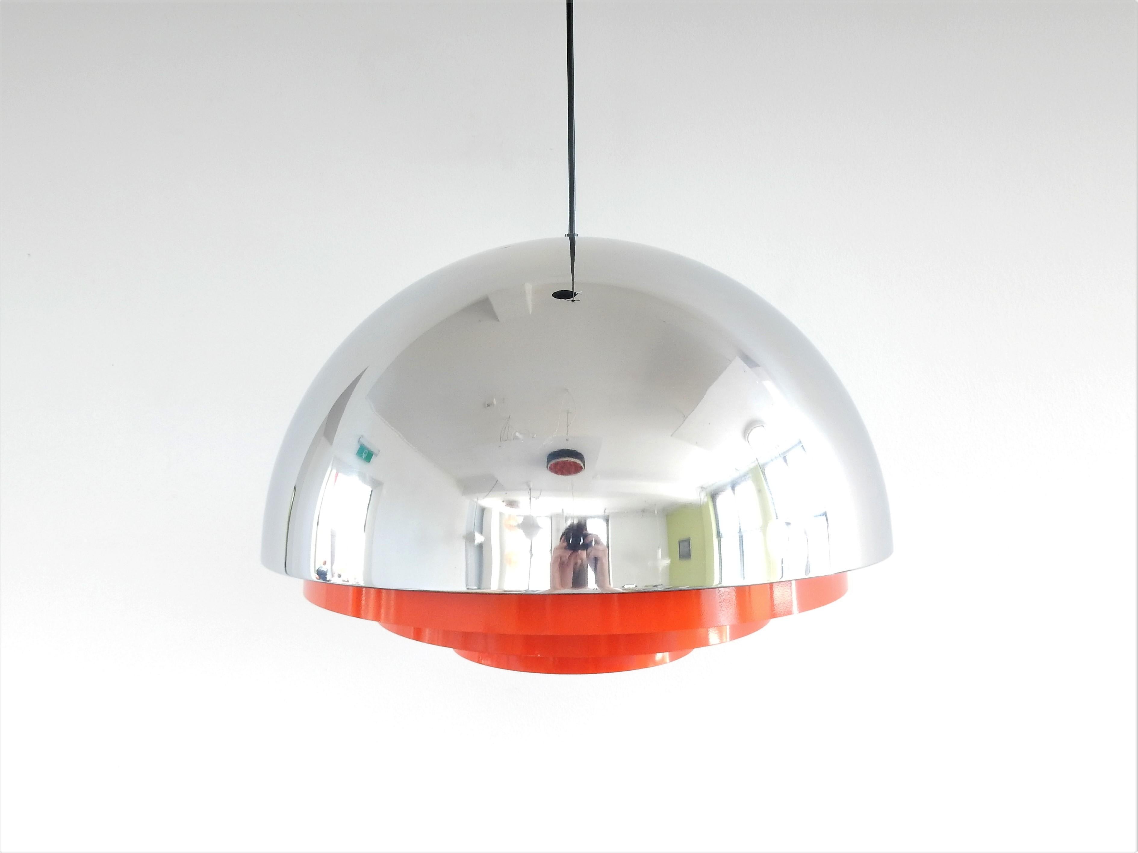 This 'Milieu Maxi' pendant lamp is a special edition from the Chrome Line series. The lamp is shaped like a half bowl, chrome plated, and it has orange metal rings and a cream inside to diffuse a soft and warm light. This lamp is in a very good and