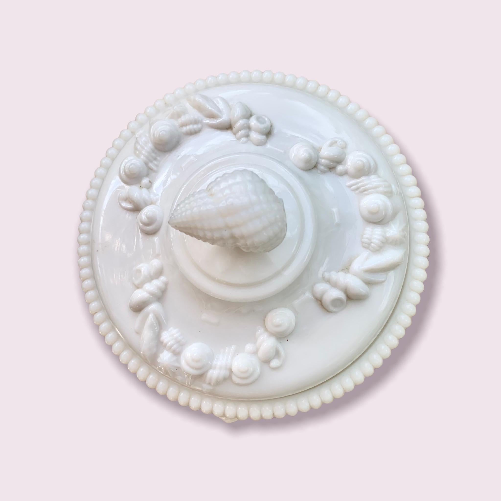 Bonbonnière en verre laiteux des années 1950 de Westmoreland, au motif Argonaut, avec de jolies guirlandes de coquillages, des perles, des pieds en forme de dauphin et une poignée en forme de coquillage. 

Fabriqué pour la première fois par