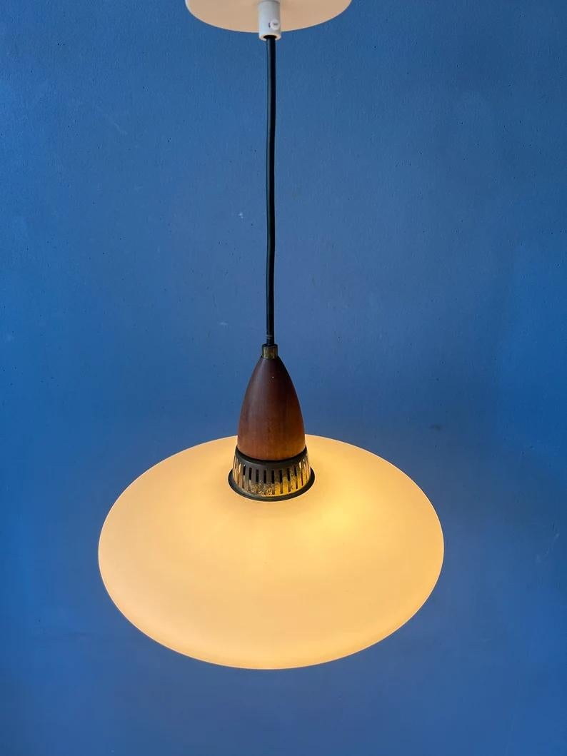 Vintage danish style milk glass pendant light with wooden top cap. The lamp has a UFO-shaped opaline glass shade and a teak wood top cap. The lamp requires an E27/26 (standard) lightbulb.

Additional information:
Materials: Glass, wood
Period: