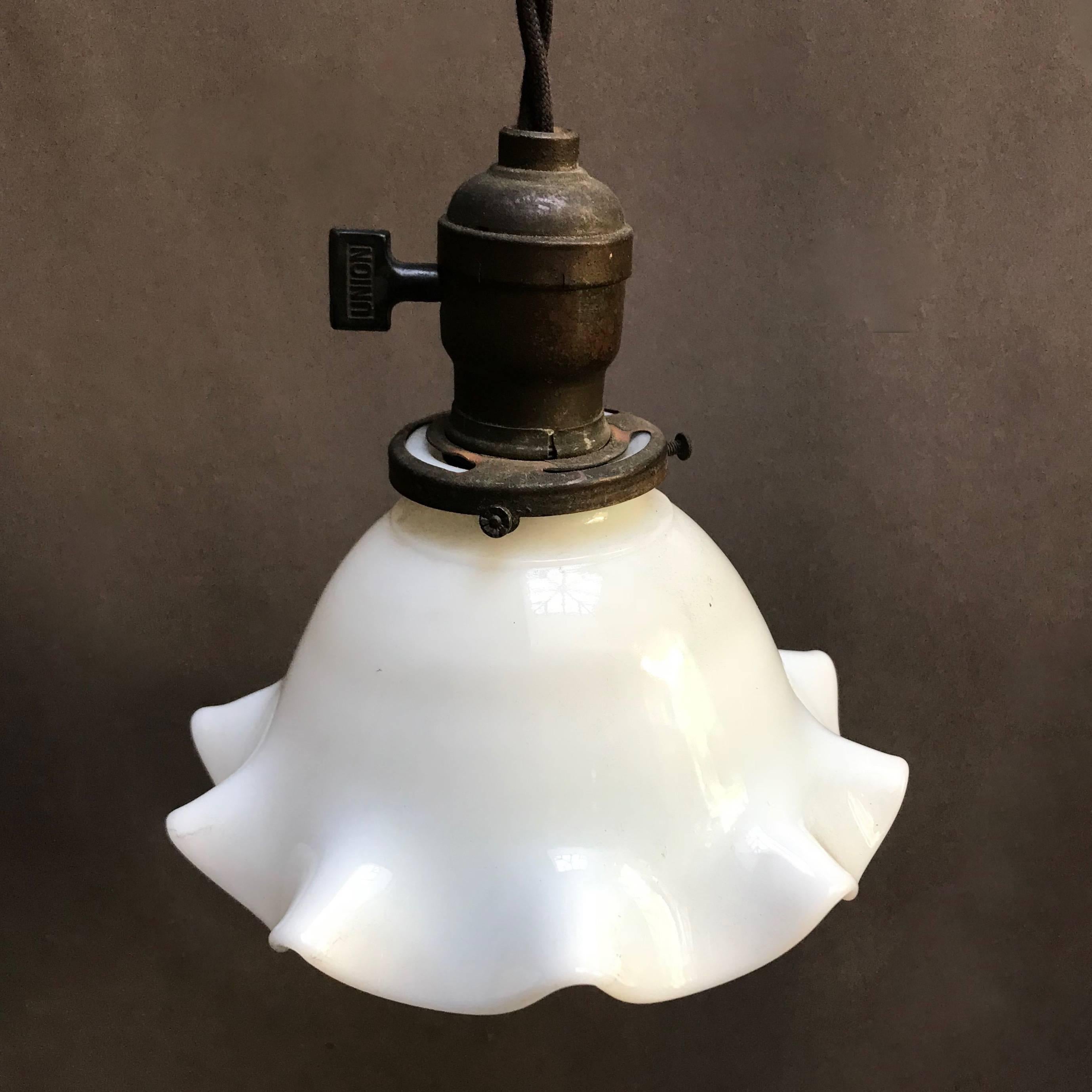 Industrial pendant light features a milk glass, bell-shape shade with pie crust ruffle edges with brass paddle switch fitter is newly wired with 48 inches of braided black cloth cord to accept a 150 watt bulb.