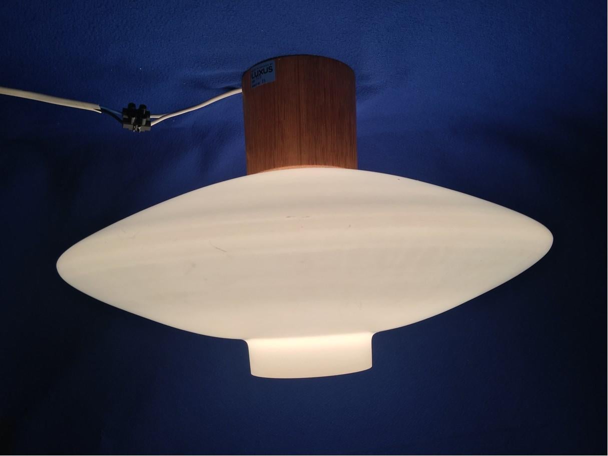 Milk glass ceiling lamp in the popular 60's UFO form with a wooden mount. From Sweden by Luxus from 1960's. The fixture requires one European E26 / E27 Edison bulbs, each bulb up to 75 watts. Rewired to meet U.S. standards.