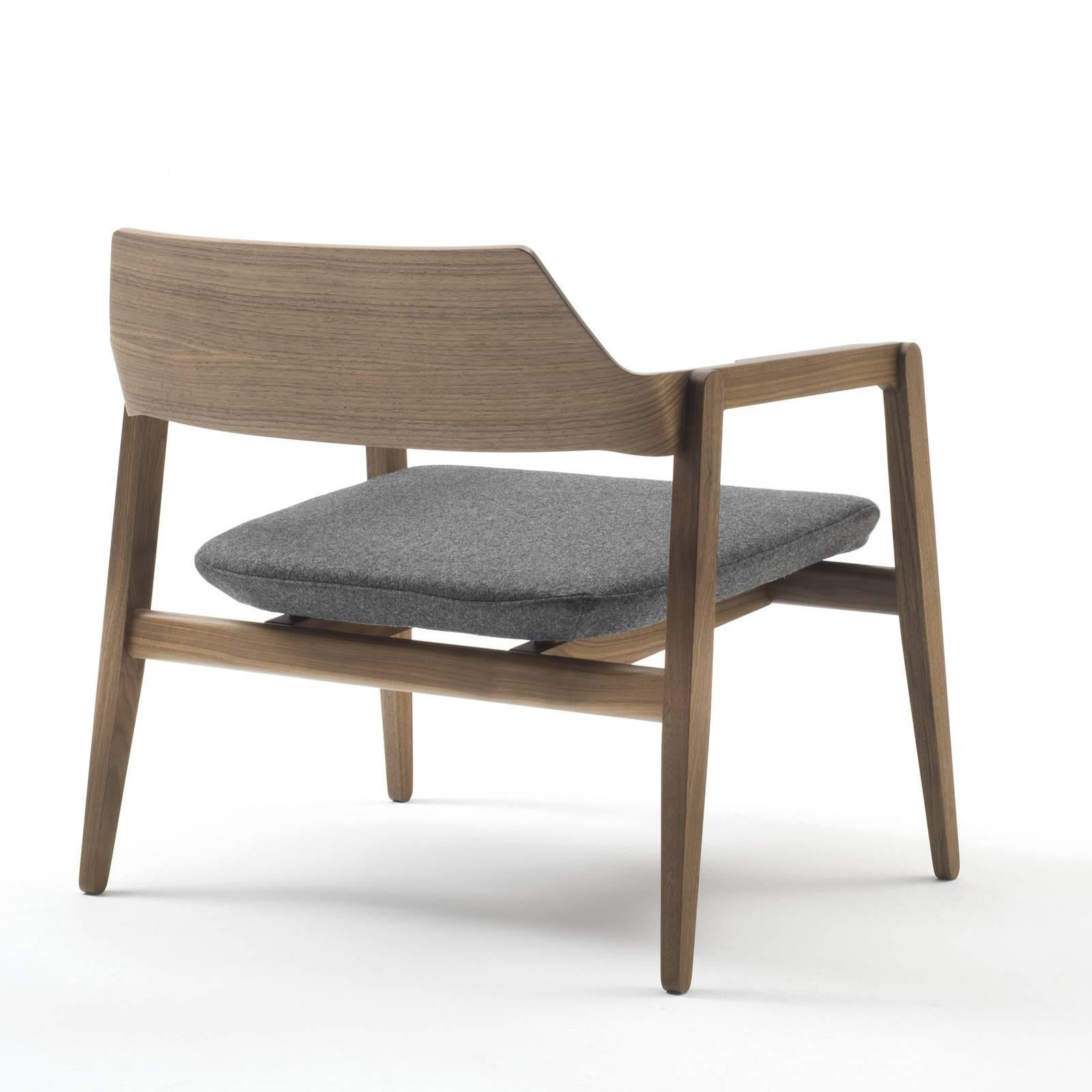 This eclectic armchair has a low and comfortable design with a curved back and a soft cushioned seat upholstered in melange gray fabric by kvadrat. The structure is made of solid oak with a natural finish with a simple yet clever aesthetic in which