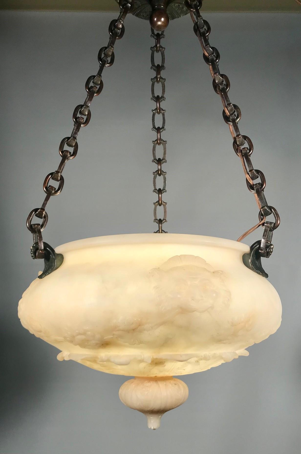 This alabaster bowl shaped fixture is carved on the sides with stylised lions and underneath with stylized acanthus. The mounting bronze hooks are modelled as fierce birds-of-prey. 

Much is made of the chain and canopy. The chain is heavy, finely