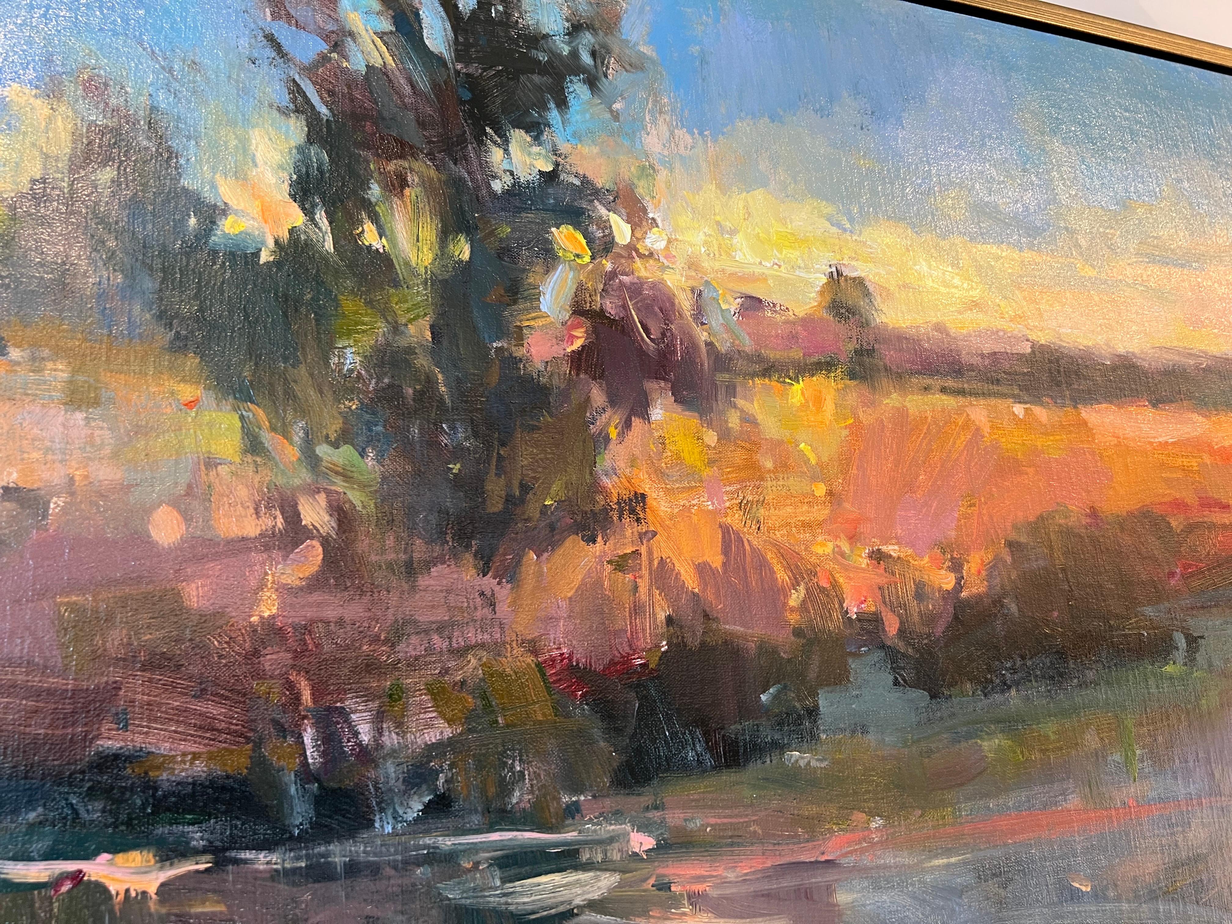 'Late Evening Lowland' is a framed Impressionist plein air landscape painting created by American artist Millie Gosch in 2022. Featuring a rich palette mostly made of blue, green, pink and orange tones, this oil on canvas painting.  Framed inside an