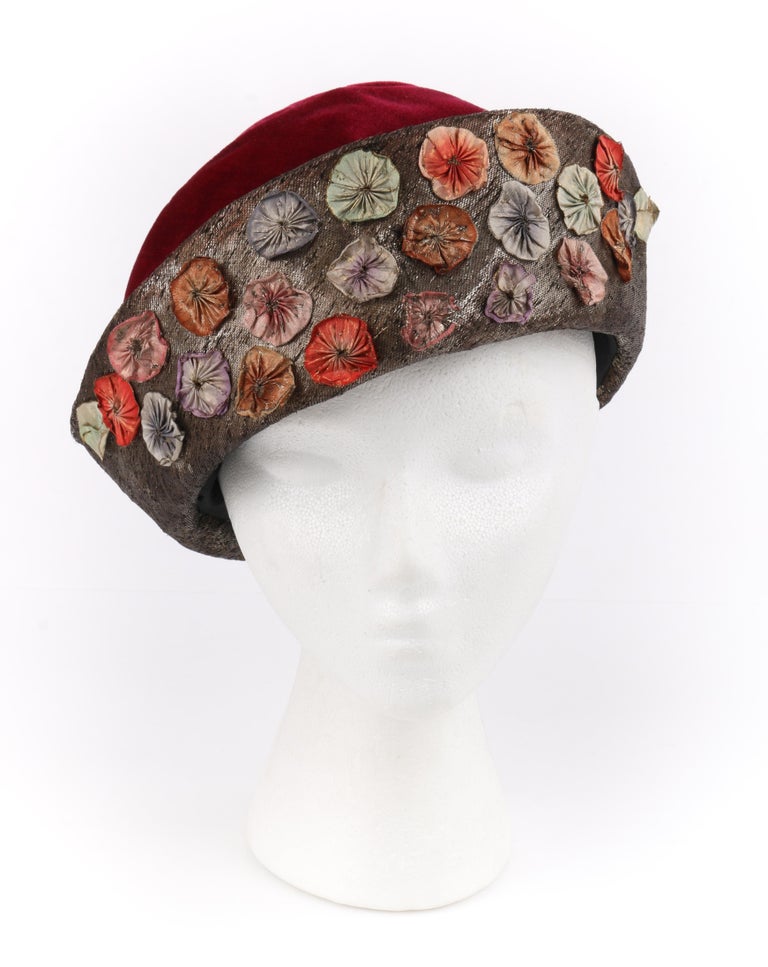 Millinery Couture c.1920s Wine Red Velvet Metallic Flower Embellished Cloche Hat

Circa: 1920’s
Label(s): Raszkowski’s Millinery
Style: Cloche hat
Color(s): Shades of garnet red, gold (body of hat); shades of pink, purple, blue, orange, red, green