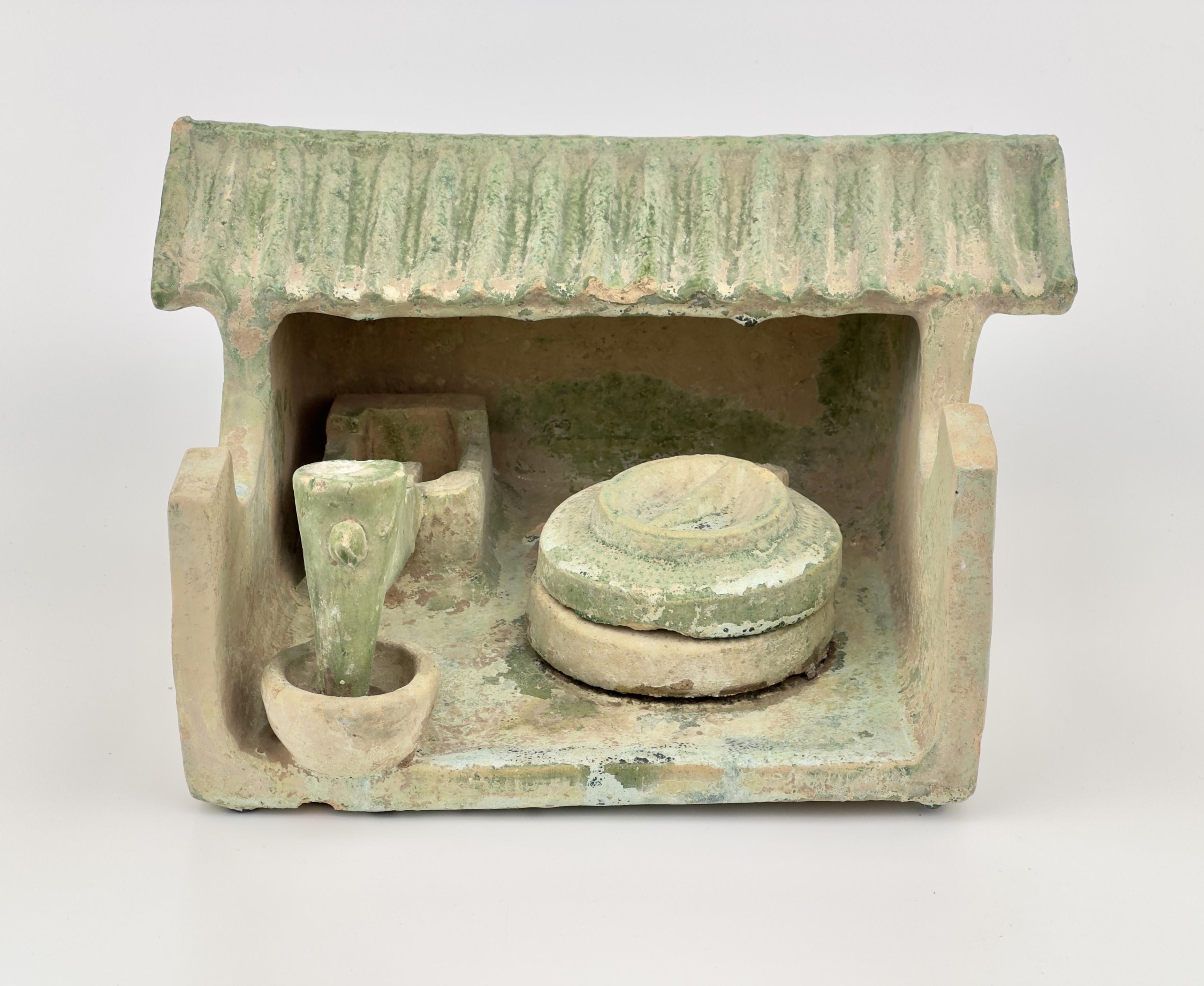Made from the standard orange earthenware body of Han green glazed tomb models, this miniature milling station features a circular millstone and a foot-operated mortar and pestle grain pounder under its shed roof. Both of these farm tools can still