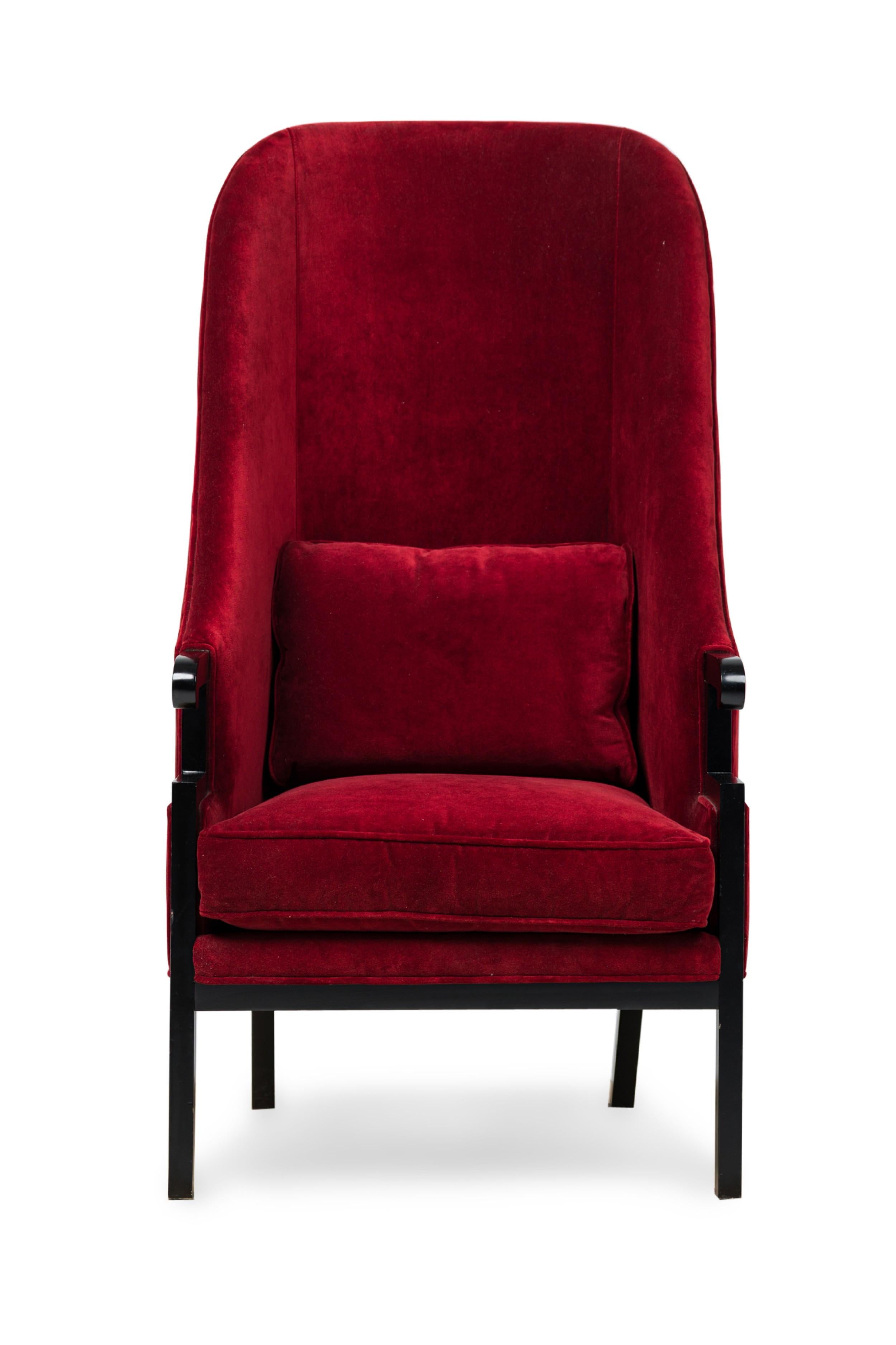 American Mid-Century black painted wooden framed armchair with an exaggerated high wing back and short curved armrests, all upholstered with a seat and throw cushion in red velvet with matching piping, resting on four square legs. (MILO BAUGHMAN)