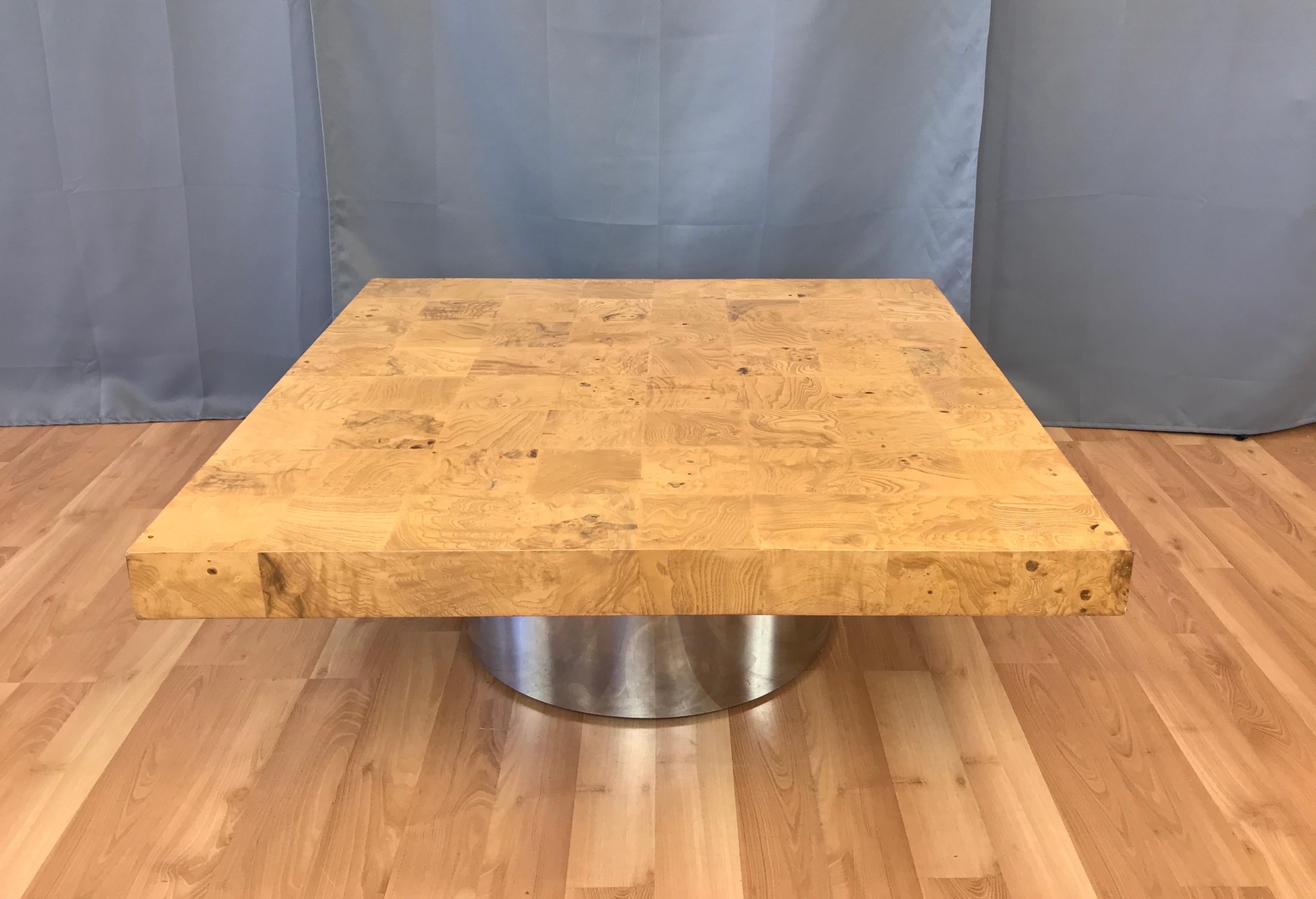 An impressive burl wood square coffee table with cylindrical metal base attributed to Milo Baughman.

Top features highly figured maple burl veneer squares, with eight to a side. Drun base is mirror polished steel. A super clean and minimalist