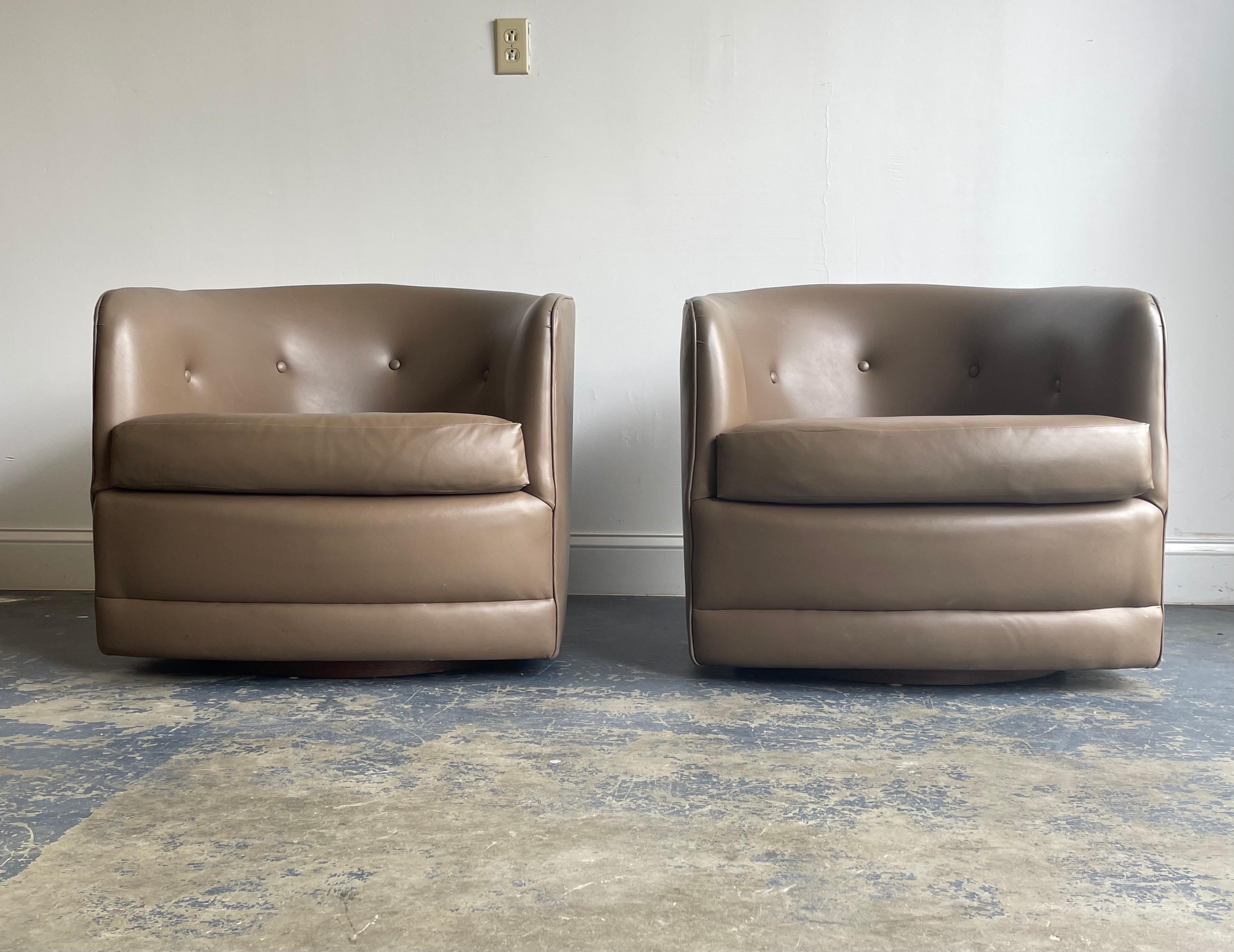 Pair of swivel and tilt club chairs attributed to Milo Baughman for Thayer Coggin. Comfortable chairs over a walnut plinth base. Upholstery appears to be a vinyl.
