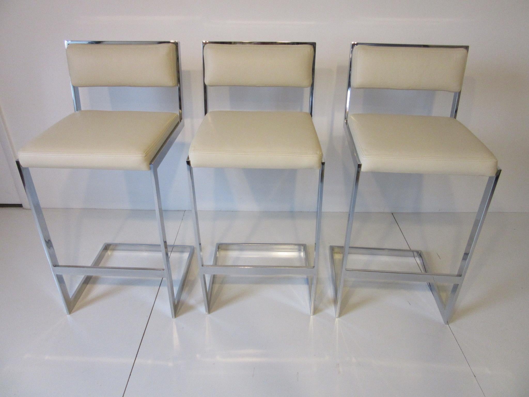 A set of three chrome bar stools reupholstered in a cream colored soft and rich leather with French double stitched seams. Manufactured by the Thayer Coggin furniture company.