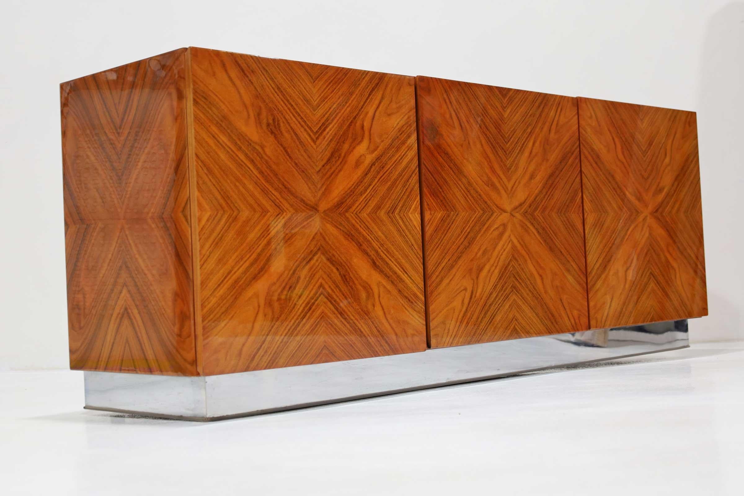 Un'imponente credenza in palissandro abbinata a libri di Milo Baughman. Questa credenza è dotata di tre ante, due delle quali si aprono per rivelare un ripiano ricco di oggetti. Un'anta si apre su quattro cassetti, due dei quali con rivestimento in