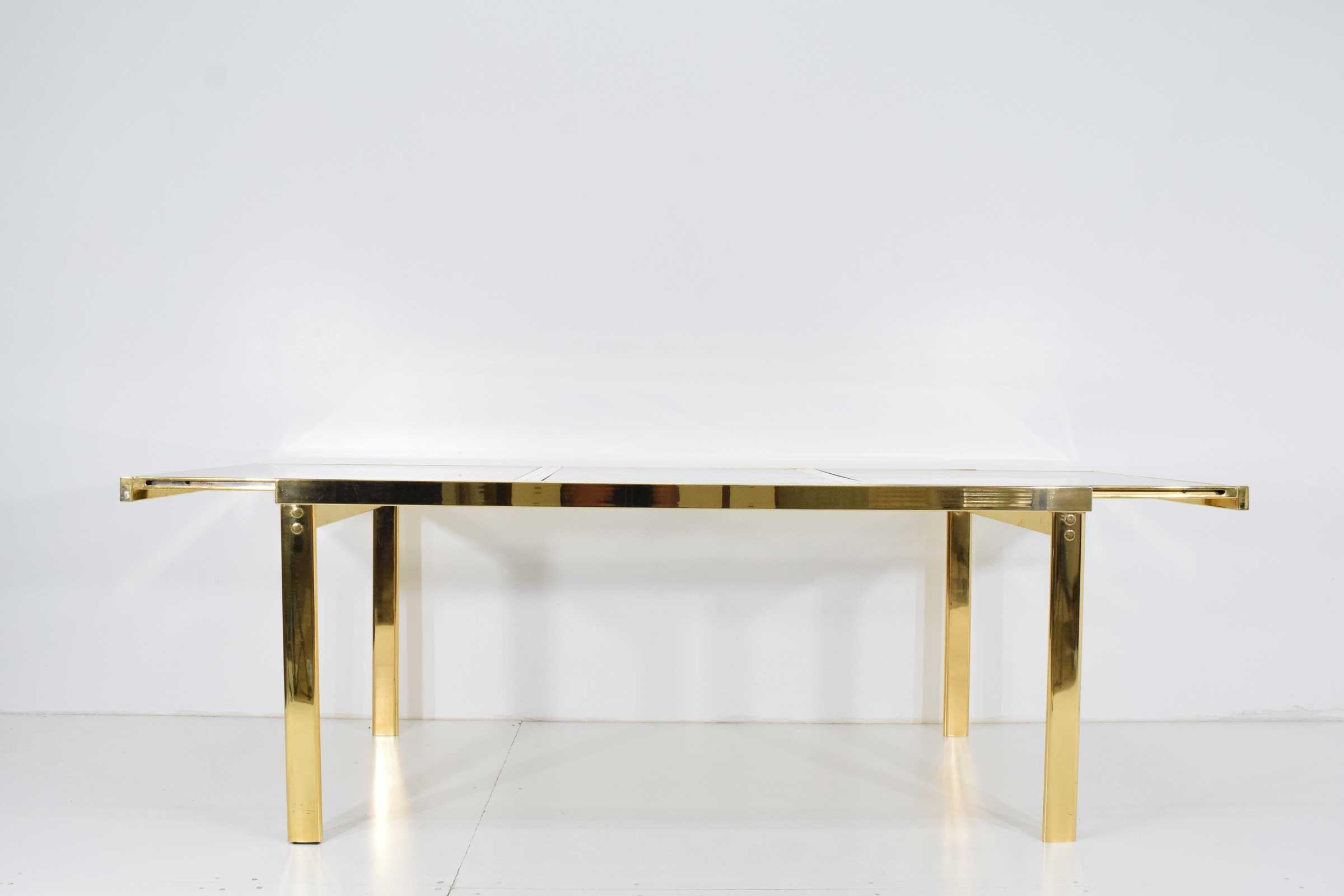 Versatile and beautiful. A brass finish extension dining table with lightly smoked glass top. See the beautiful brass frame dining chairs that came with this set in our storefront listings. I included an image. Measures: 94