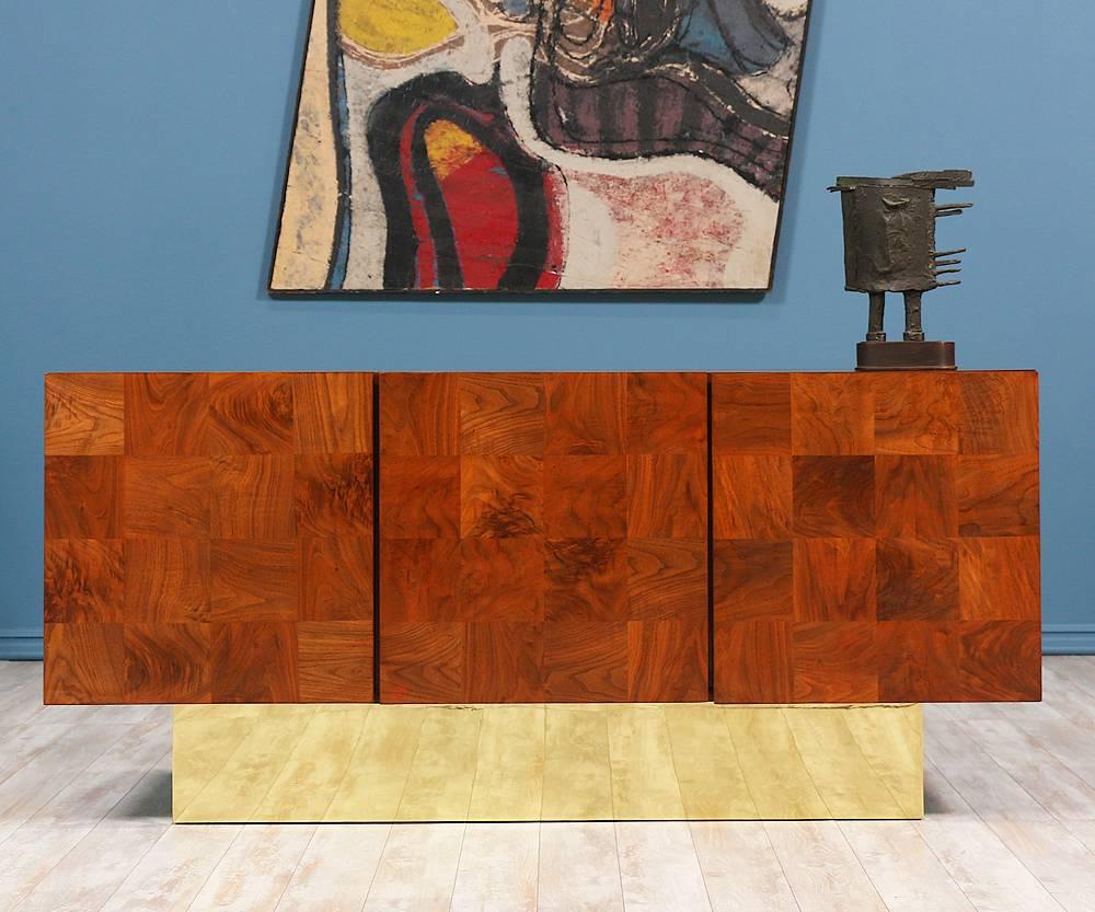 Extraordinary Milo Baughman credenza designed for Thayer Coggin in the 1960’s. Sitting on a polished lightly and patinated brass plinth base, the checkered burl wood designed case features three doors with two compartments that lie behind. Behind