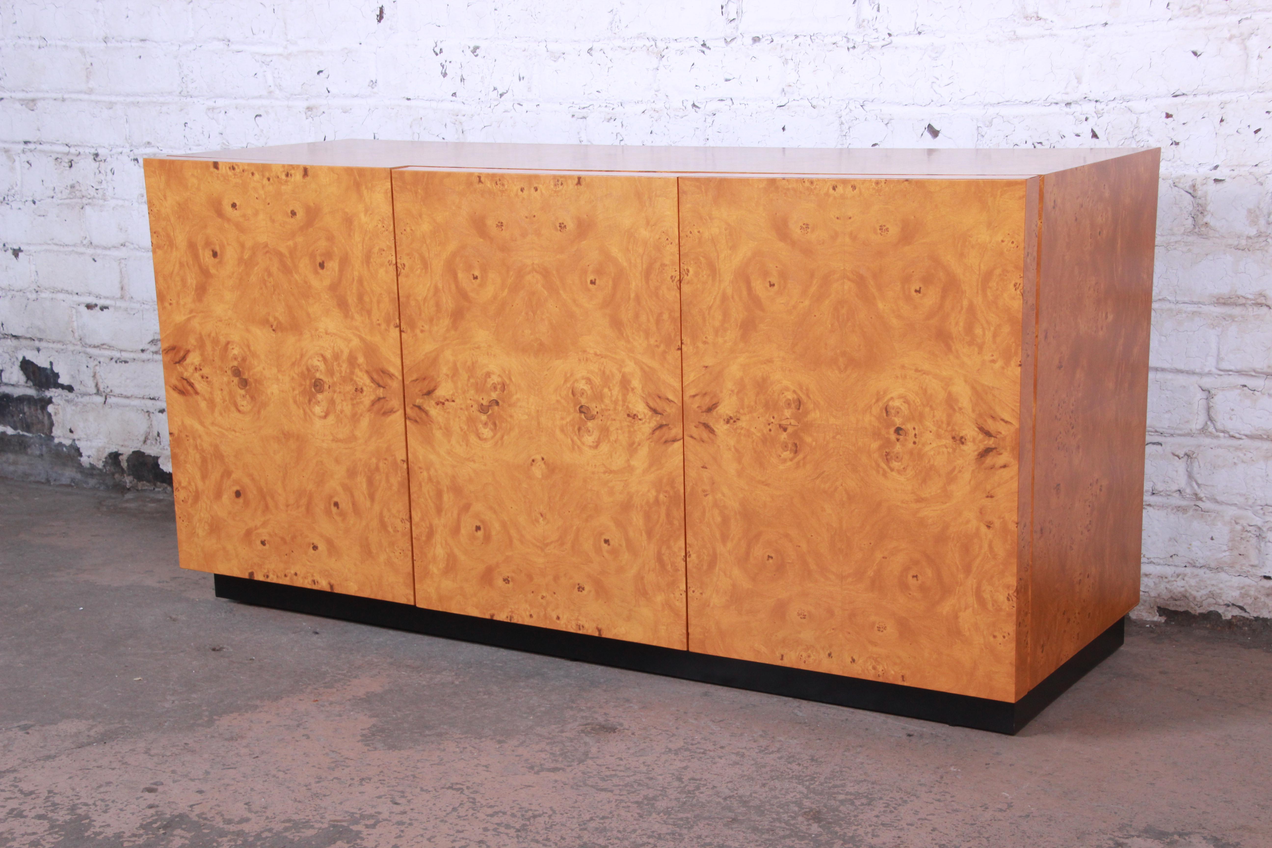 An exceptional Mid-Century Modern burled olive wood credenza or sideboard designed by Milo Baughman. The credenza features gorgeous burled wood grain, a nice black plinth base, and sleek midcentury design. It offers ample room for storage, with two
