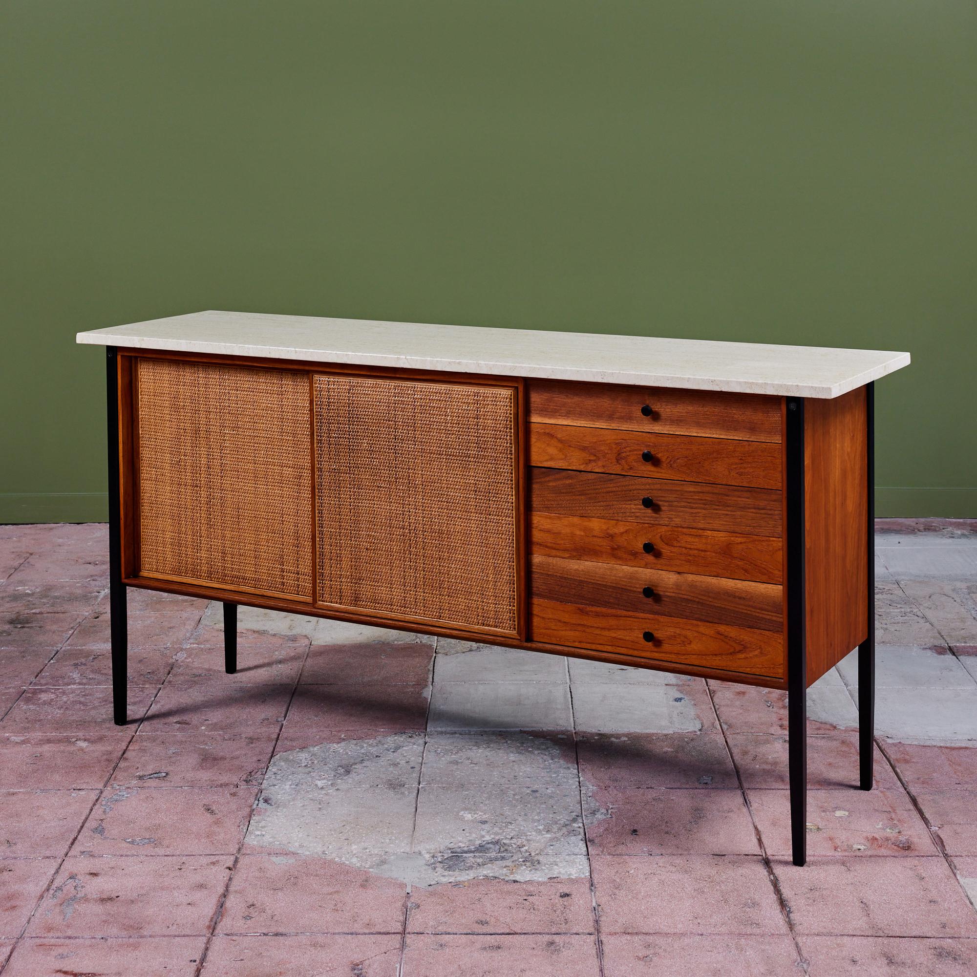 Milo Baughman for Arch Gordon credenza, USA, c.1950s. The cabinet features an oiled walnut frame, painted metal legs and drawer pulls, polished travertine top, and sliding doors with cane panels.

Dimensions
66” width x 18” depth x 33.25”