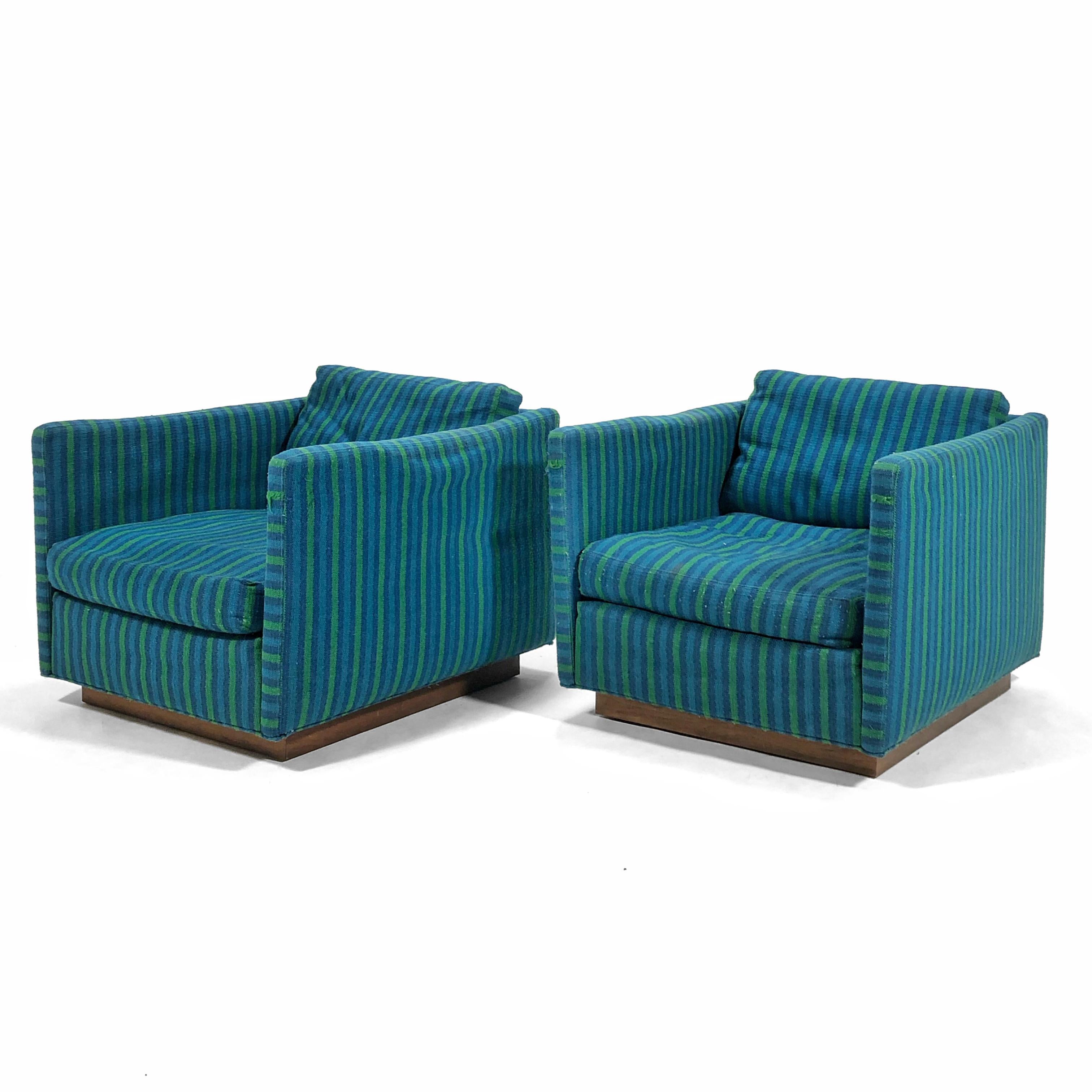 This handsome pair of tuxedo or cube lounge chairs designed by Milo Baughman for James Inc. feature clean  lines and walnut plinth bases.

The original blue and green striped upholstery could be retained or replaced, but the internal foam and