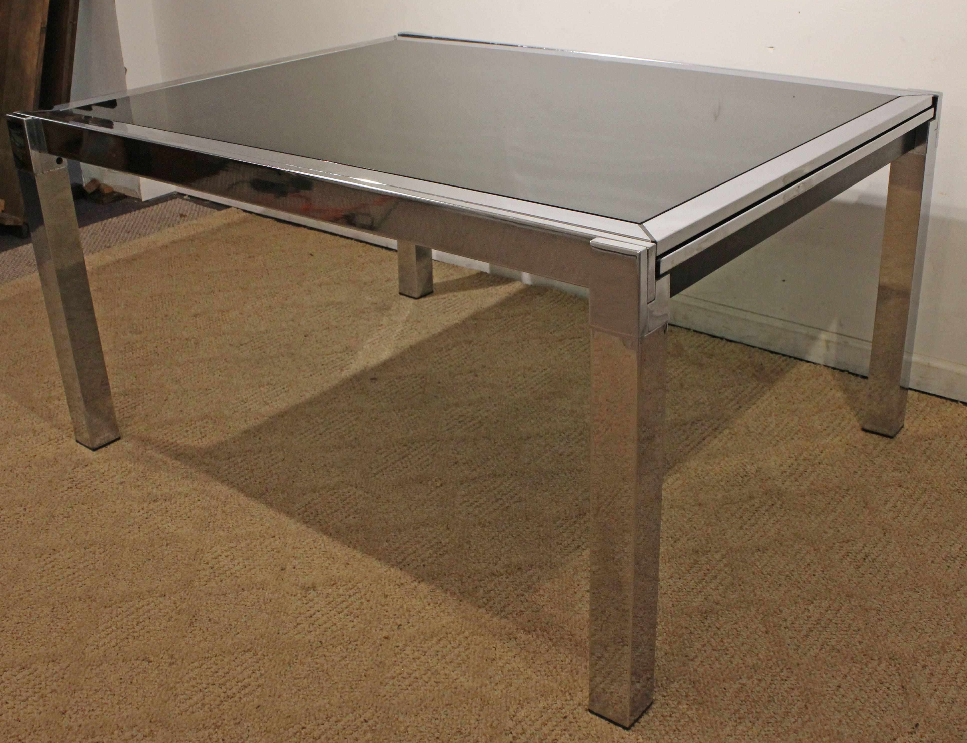 Offered is a chrome extension dining table attributed to Milo Baughman for D.I.A (Design Institute of America). This table is made of chrome with black glass. Has two hidden extensions under the tabletop. It is not signed.

Dimensions:
without