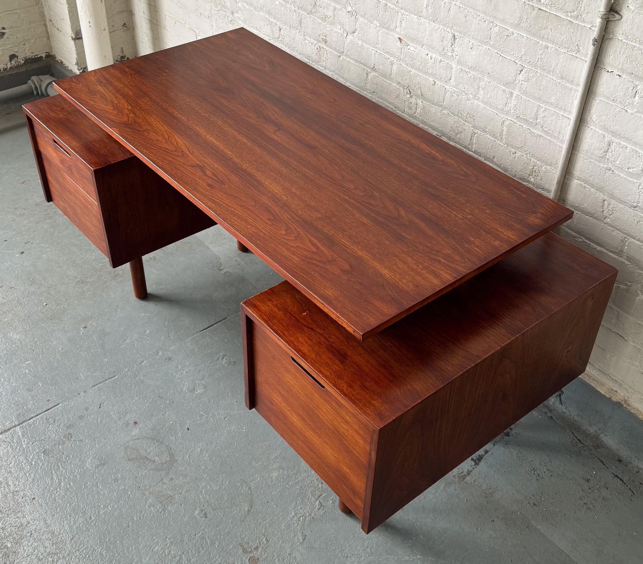 Desk in walnut with floating top, flanking drawers on the front, and a rectangular open space for display or storage at the rear, supported on four cylindrical legs. An architecturally resonant Milo Baughman design, model 1625, produced by Glenn of