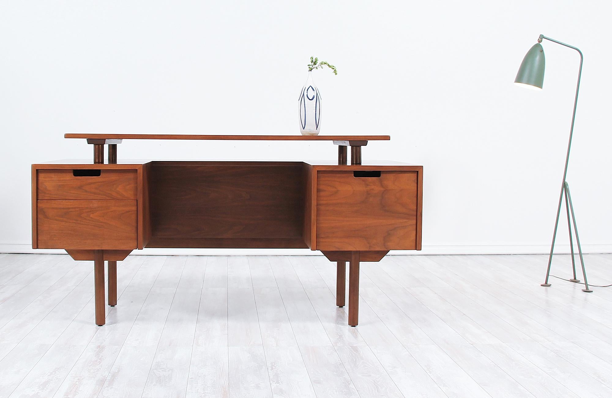 Mid-Century Modern desk designed by Milo Baughman for Glenn of California in the United States circa 1950s. This exceptionally crafted modern desk features a sturdy walnut wood frame with four cylindric feet and three front drawers with an open back