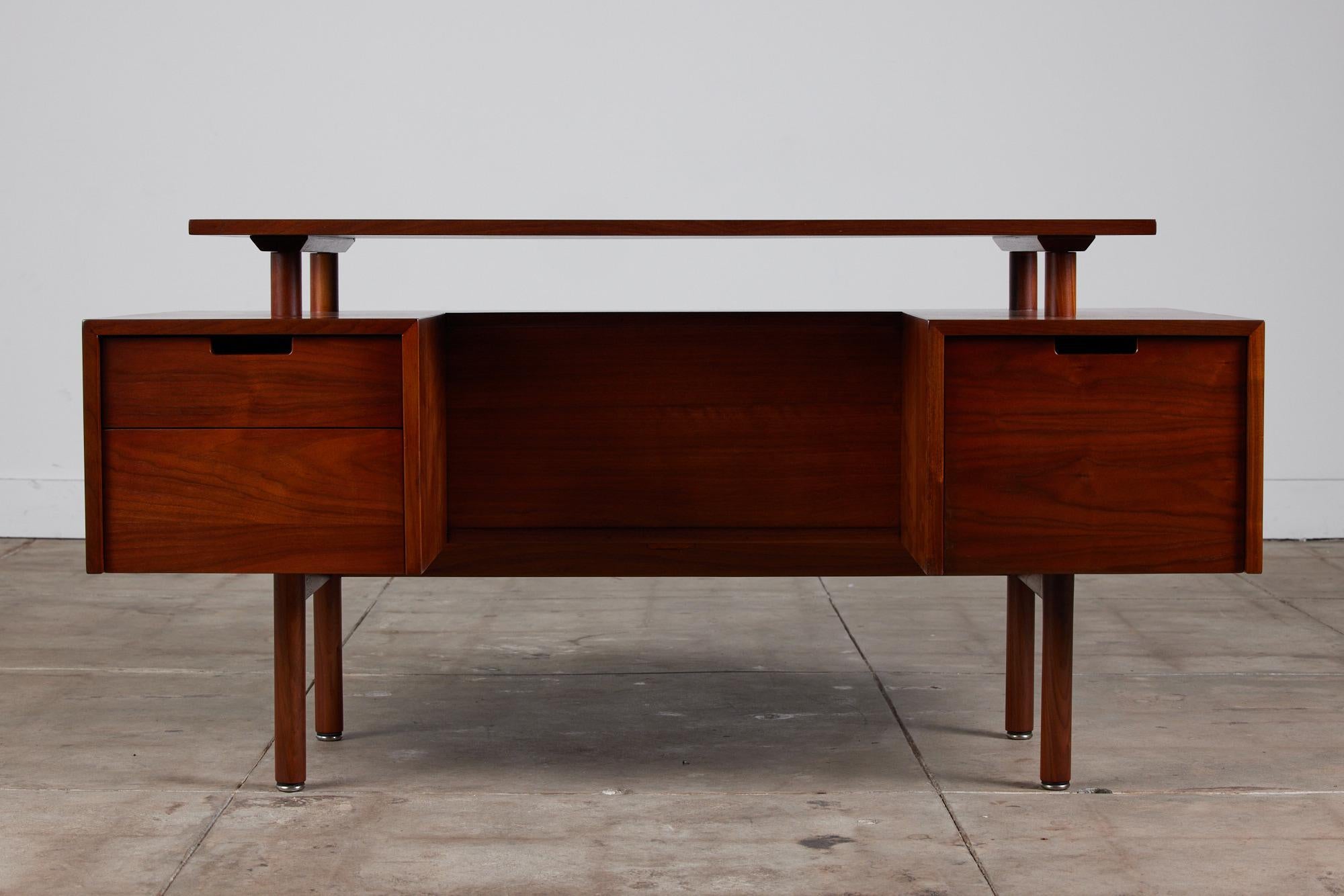 Classic California design, c.1950s, a walnut executive desk with a broad floating writing surface by Milo Baughman. This piece features three storage drawers, one large one and two smaller drawers. The front of the desk showcases a shelf that runs