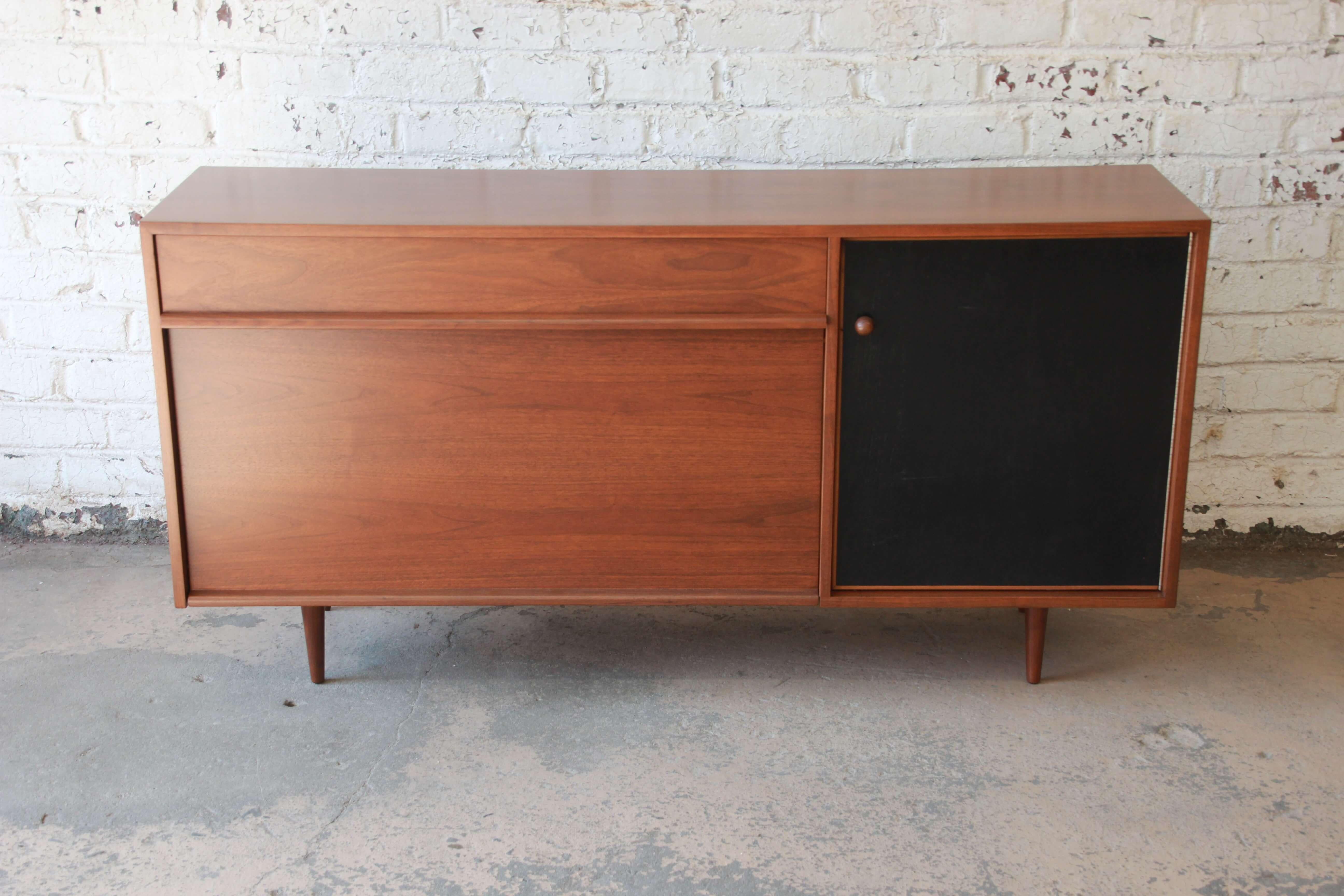 Offering a very nice walnut sideboard credenza by Milo Baughman for Glenn of California. The credenza has a very nice walnut wood grain with an ebonized black cabinet door to the right. The door opens up to a drawer at top with a shelf and two