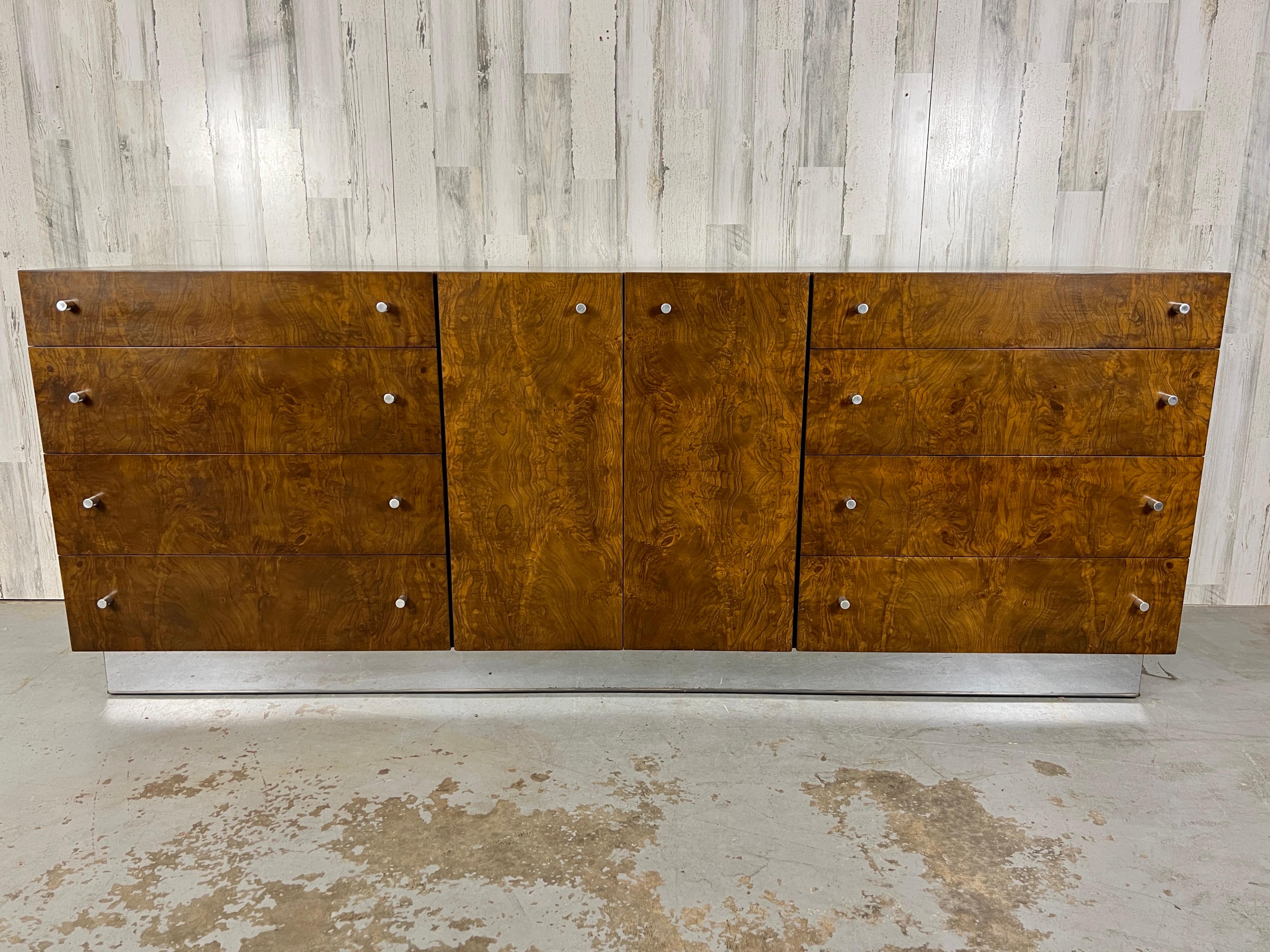 Milo Baughman for Thayer Coggin Burl & Chrome Dresser. The dresser is a true mid-century classic with 8 drawers and 2 doors, providing ample storage space. Adorned with beautiful burl wood on all sides and a chrome plinth, it combines both