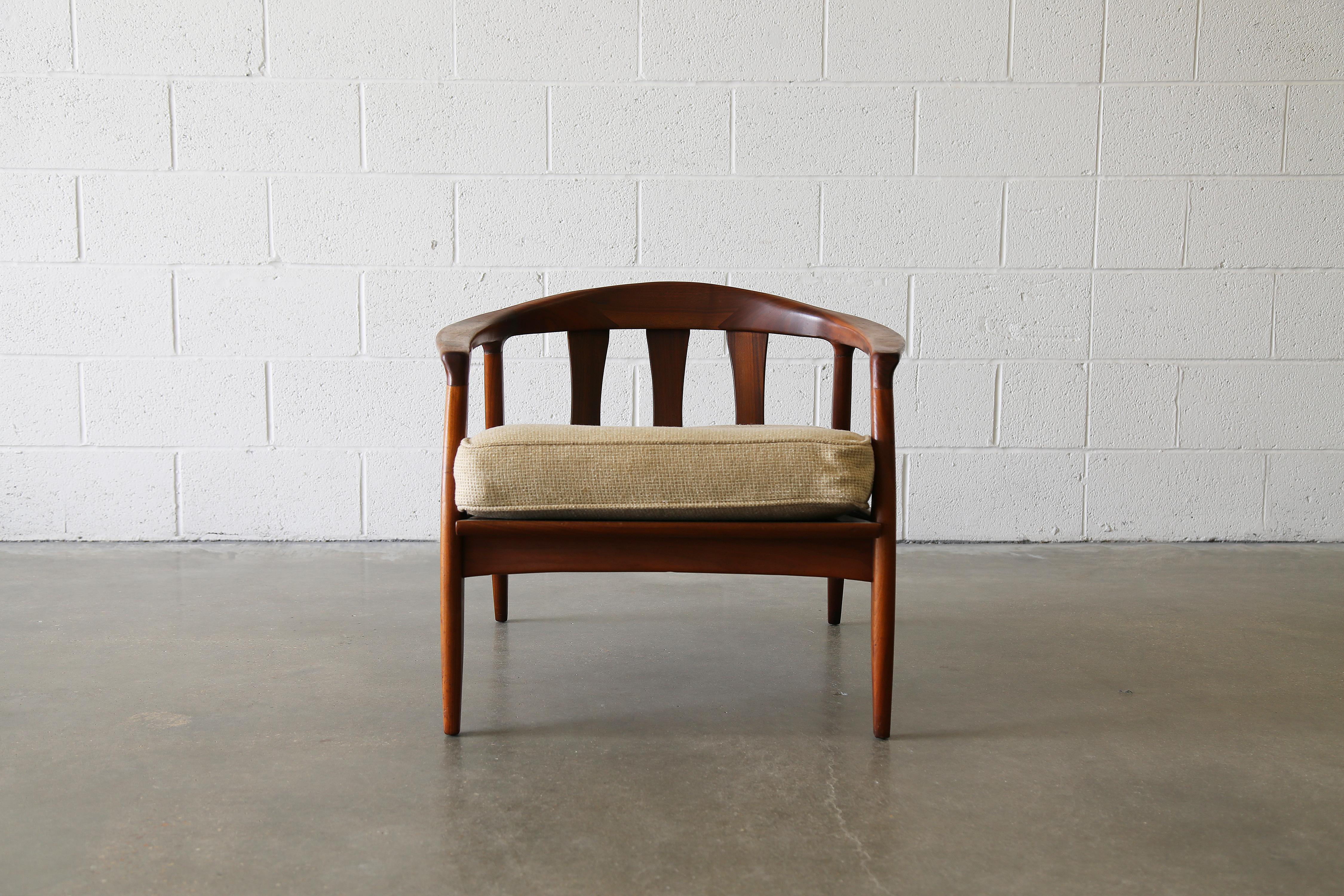 A solid walnut mid century modern lounge chair designed by Milo Baughman for Thayer Coggin, circa 1960s. Featuring a low arched sculptural back with forward slanting legs, the chair has a lot of visual movement. Shown with a seat cushion, a loose