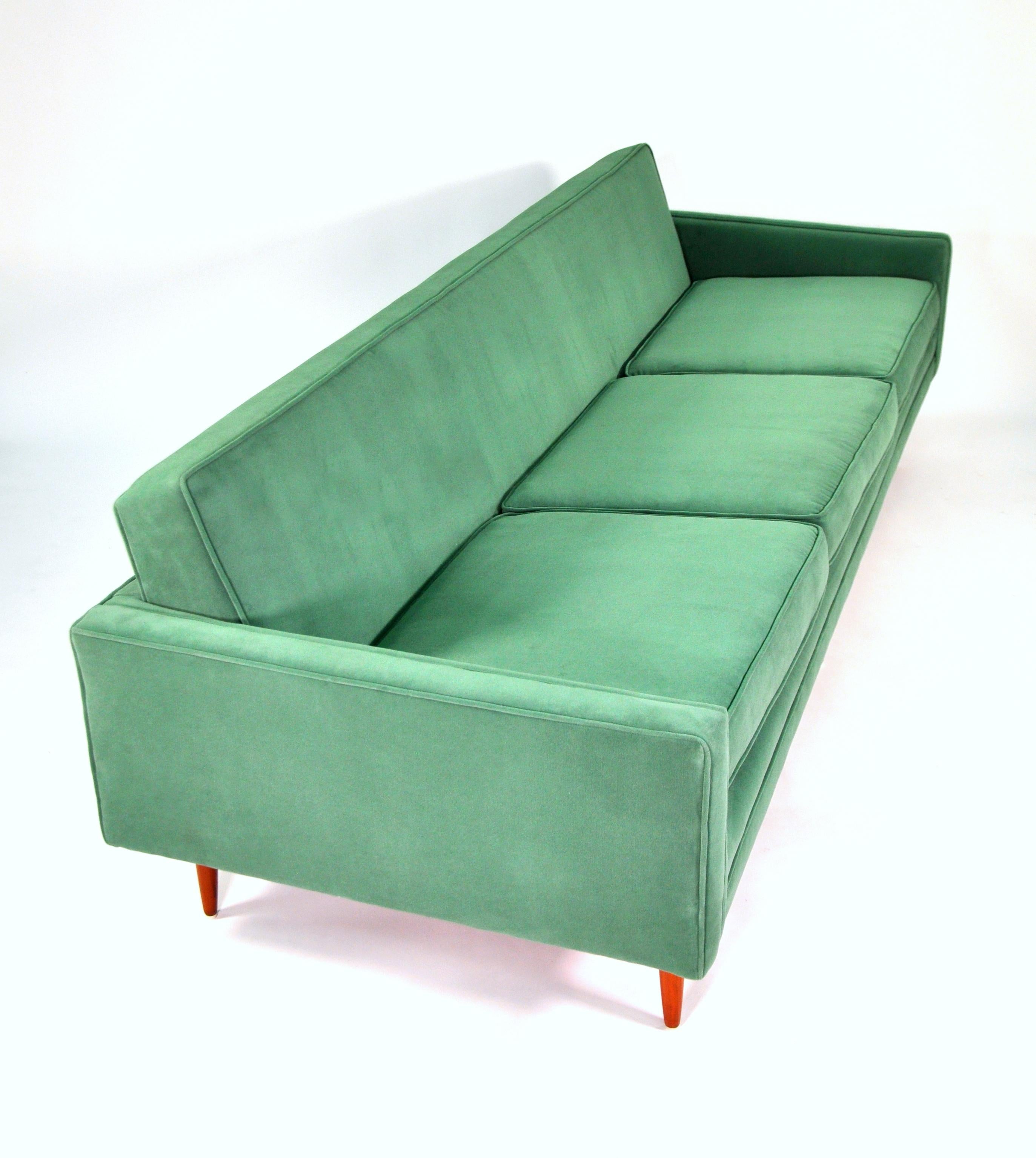 A Mid-Century Modern couch with walnut legs, dating from the 1950s and newly reupholstered in a light emerald green cotton velvet. The vintage three-seat sofa, designed by Milo Baughman for Thayer Coggin, features loose cushions and round tapered