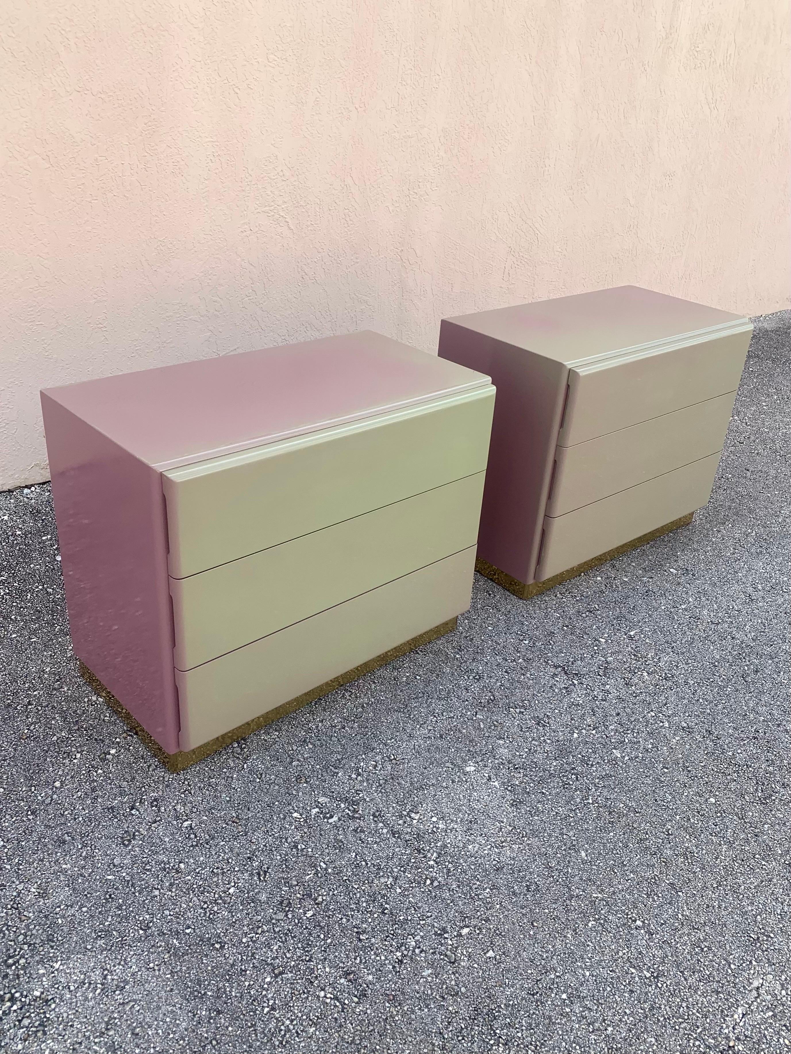 A beautiful and unique pair of nightstands designed by Milo Baughman for Thayer Coggin. Lacquer finished wood atop a brass plinth base. Three spacious drawers in each. 

Sporting an one of a kind finish. They were originally all the jade color but