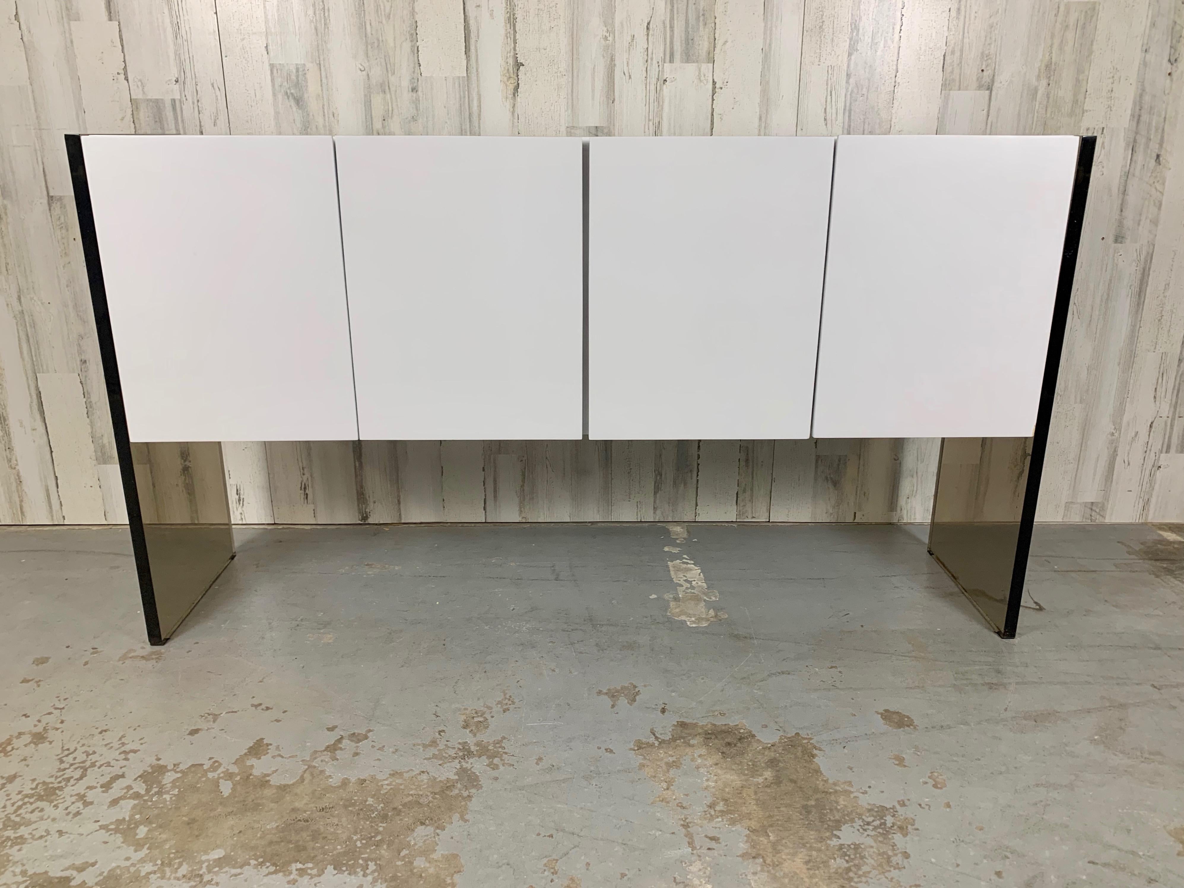 Smoked lucite anchored to a matte white four door cabinet for that floating affect. Designed by Milo Baughman for Thayer Coggin 1970s.
