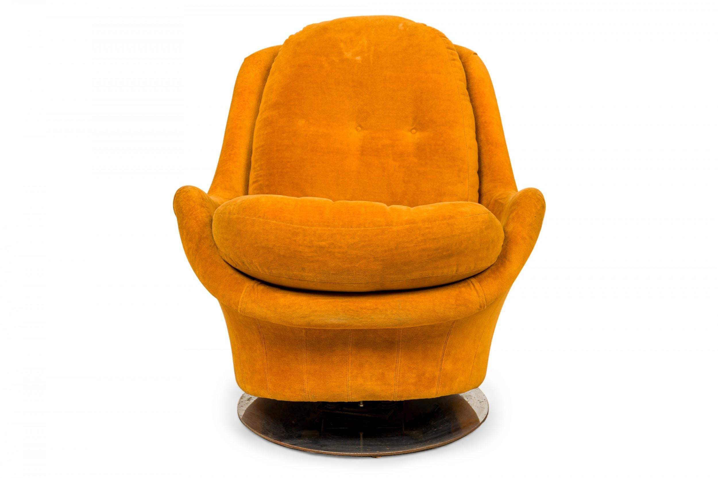 Fauteuil de salon américain de style Space Age, pivotant et inclinable, tapissé de velours orange doré avec des boutons sur le coussin du dossier, reposant sur une base circulaire en métal. (MILO BAUGHMAN POUR THAYER COGGIN).
 