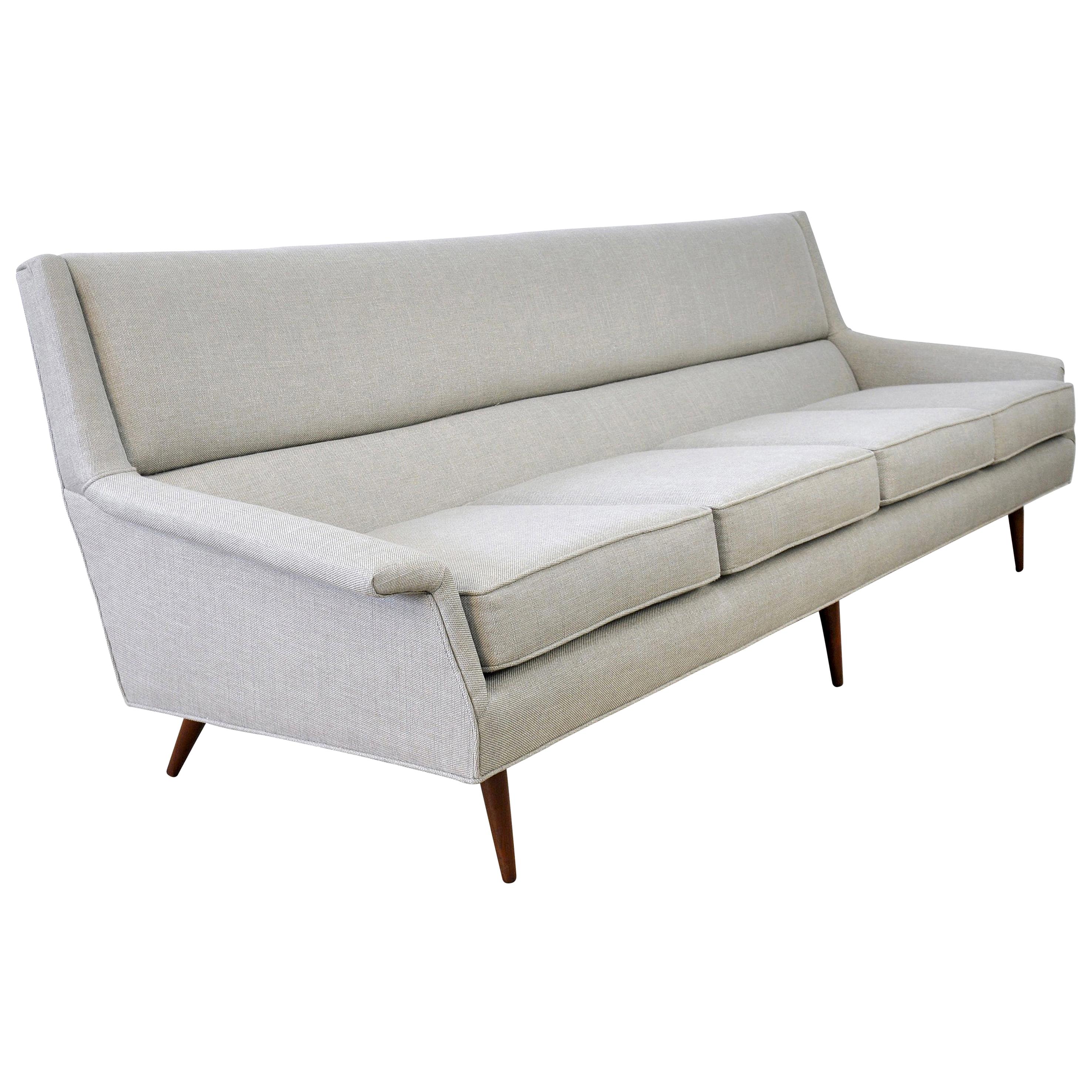 A sleek Mid-Century Modern light grey couch with walnut tapered legs, newly reupholstered in an overcast gray fabric with silver and beige undertones. The vintage four-seat sofa, dating from the 1950s, was designed by Milo Baughman for Thayer Coggin