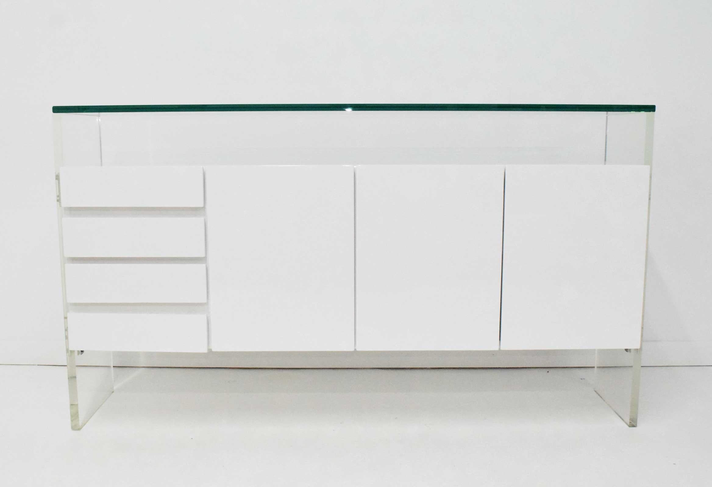 One of his iconic designs, a restored in white lacquer sideboard by Milo Baughman. Sideboard features a floating case piece that includes three doors with shelving and silverware storage. On the left side is four drawers. The thick Lucite legs