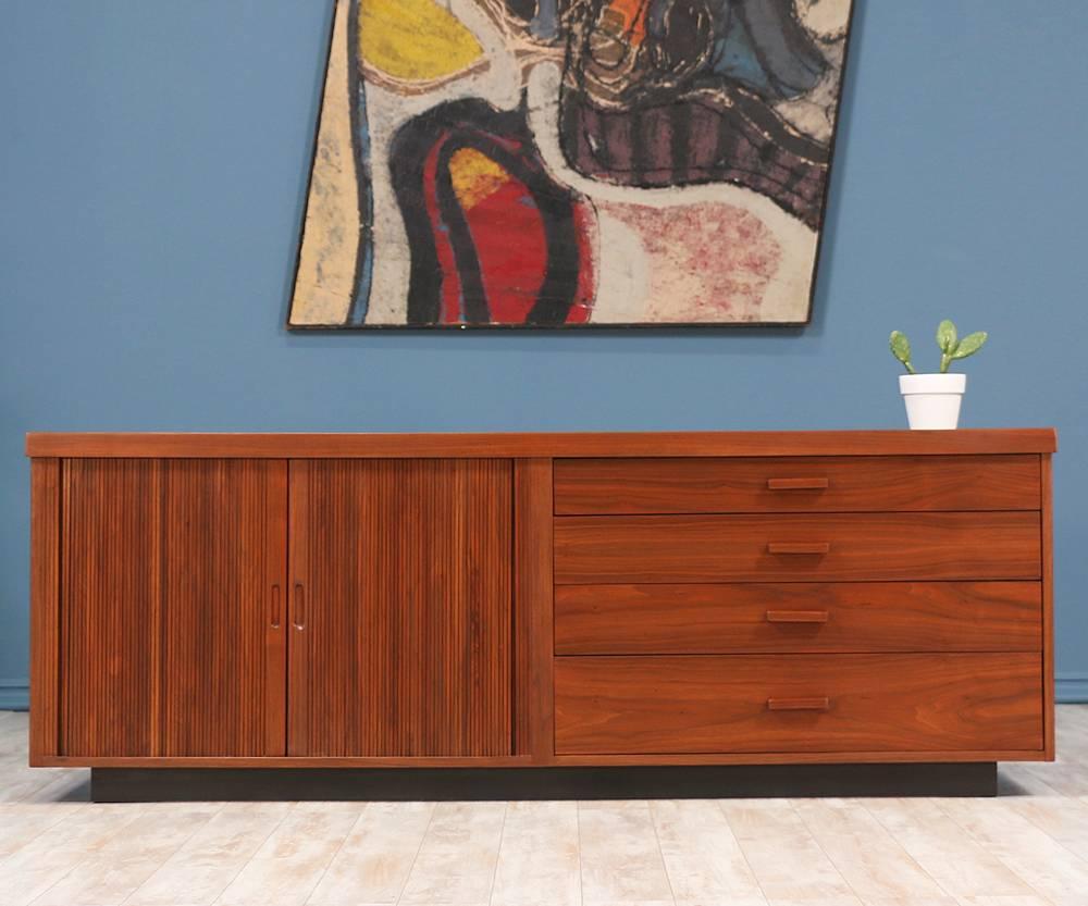 Mid Century Modern Credenza designed by Milo Baughman for Glenn of California in the United States c. 1950’s. This beautiful storage piece is comprised of walnut wood. The left side features two tambour doors with recessed pulls that reveal a
