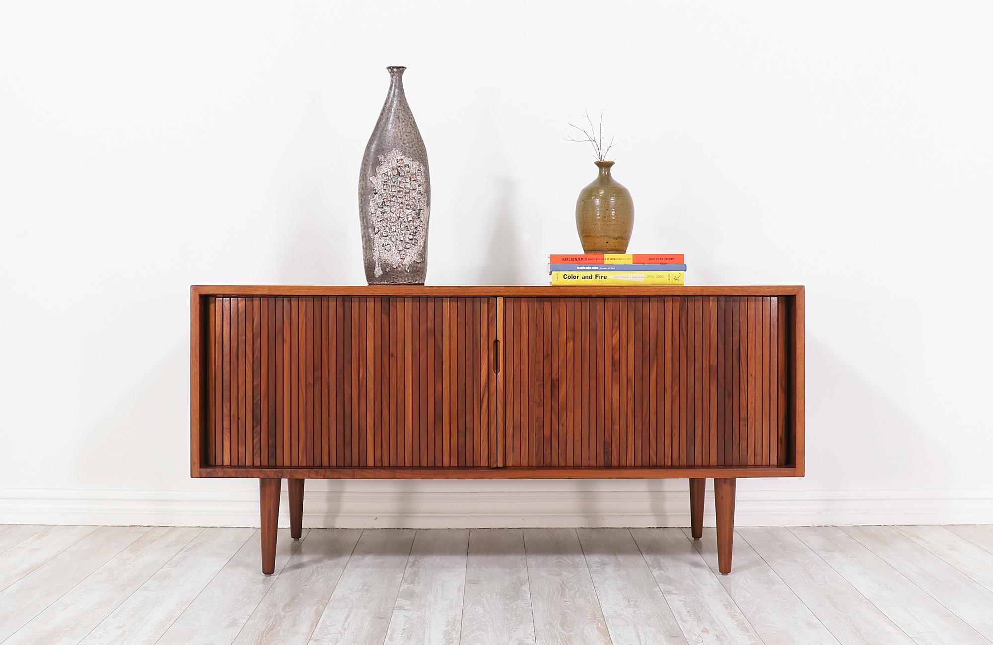 Mid-Century Modern low credenza designed by Milo Baughman for Glenn of California in the United States, circa 1950s. This exceptional credenza features a sturdy walnut wood construction with four interior compartments, a set of tambour doors with