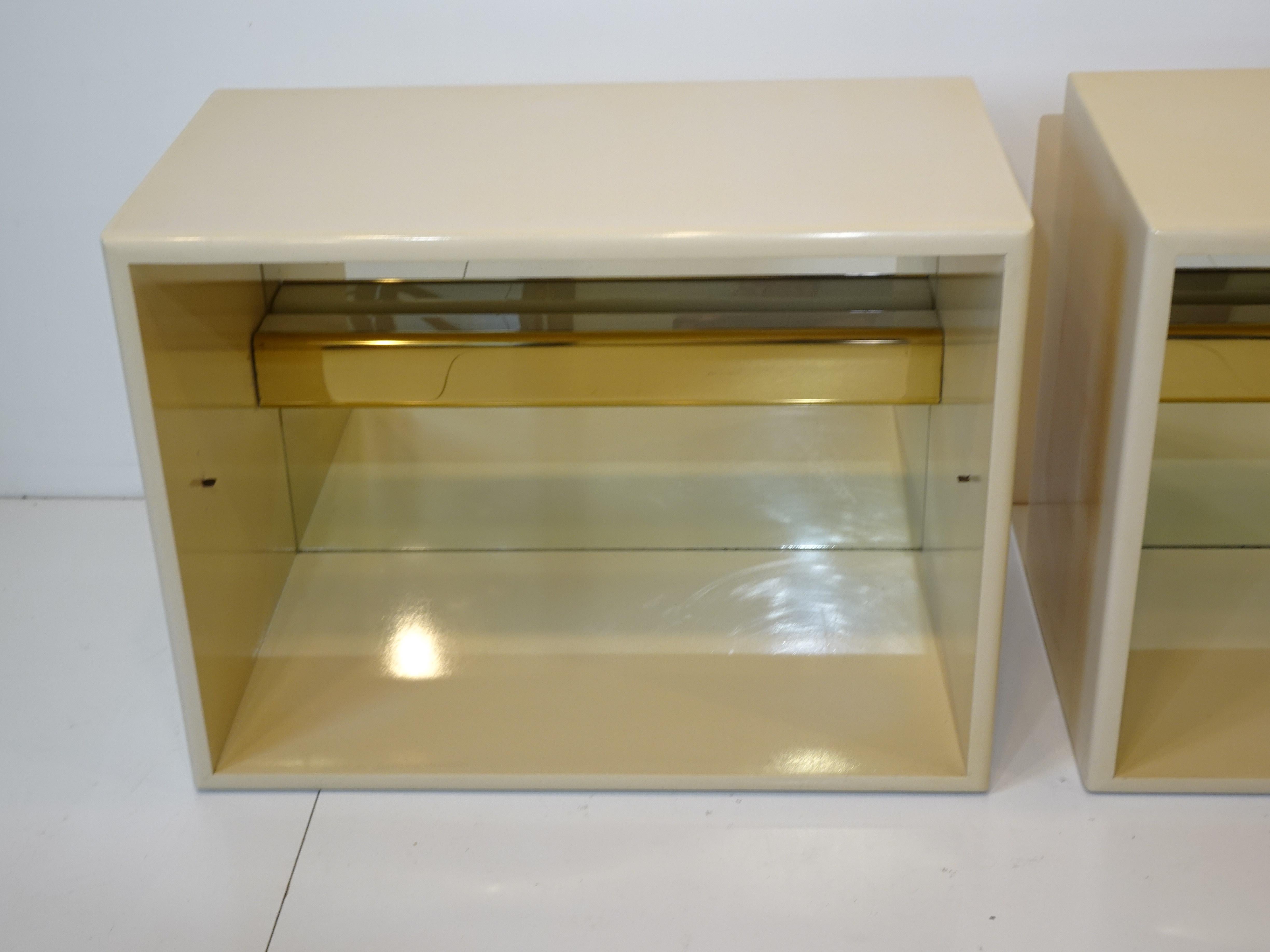 A pair of bone white nightstands with adjustable glass center shelve and a brass light having up and downward lighting with mirrored back. Retains the manufactures label Thayer Coggin designed by Milo Baughman.