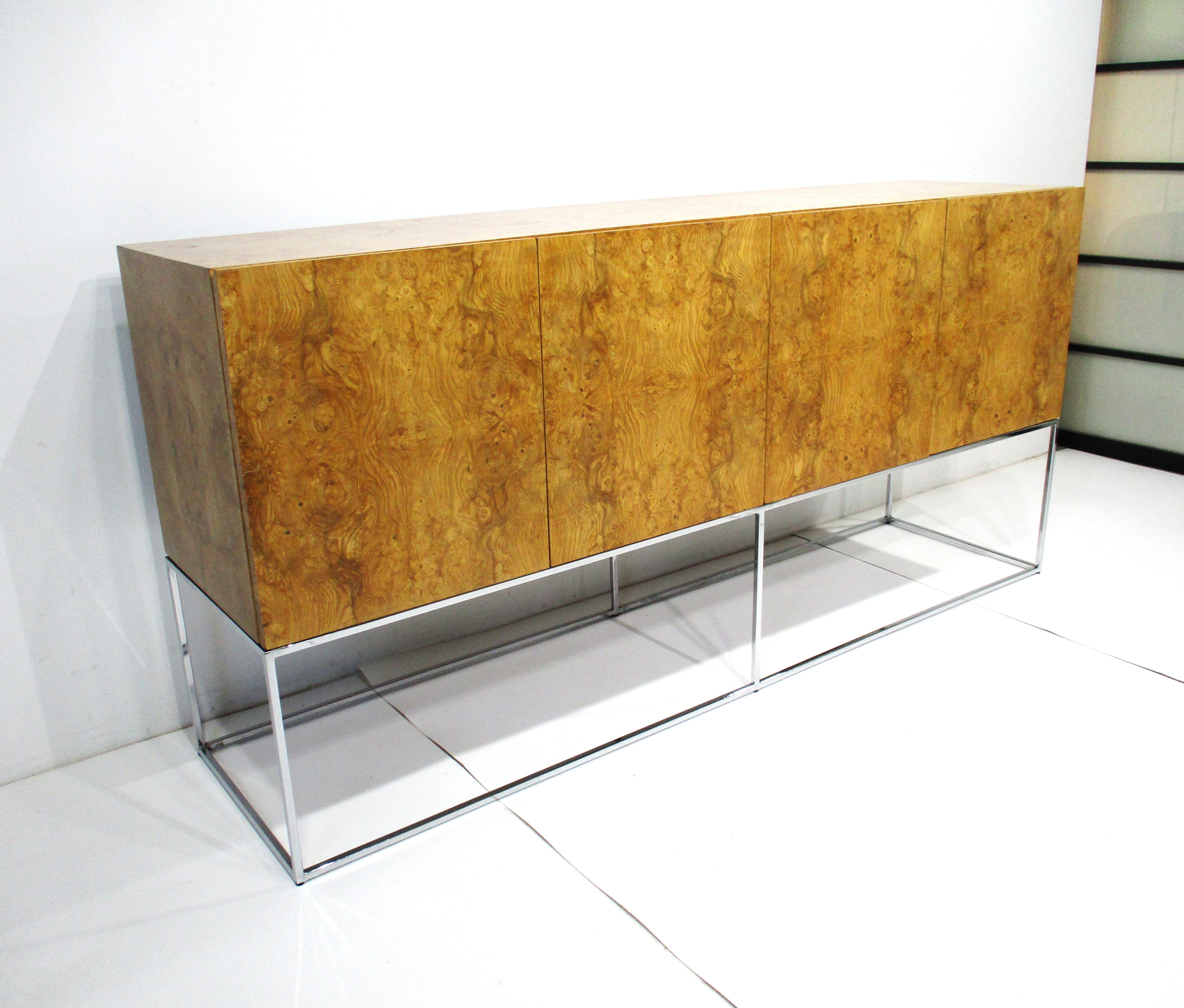 A beautifully book matched four door olive burlwood credenza or server floating on a polished chrome squared tubed steel base having two drawers and storage with two adjustable shelves. By Milo Baughman this is one of his most sought after designs