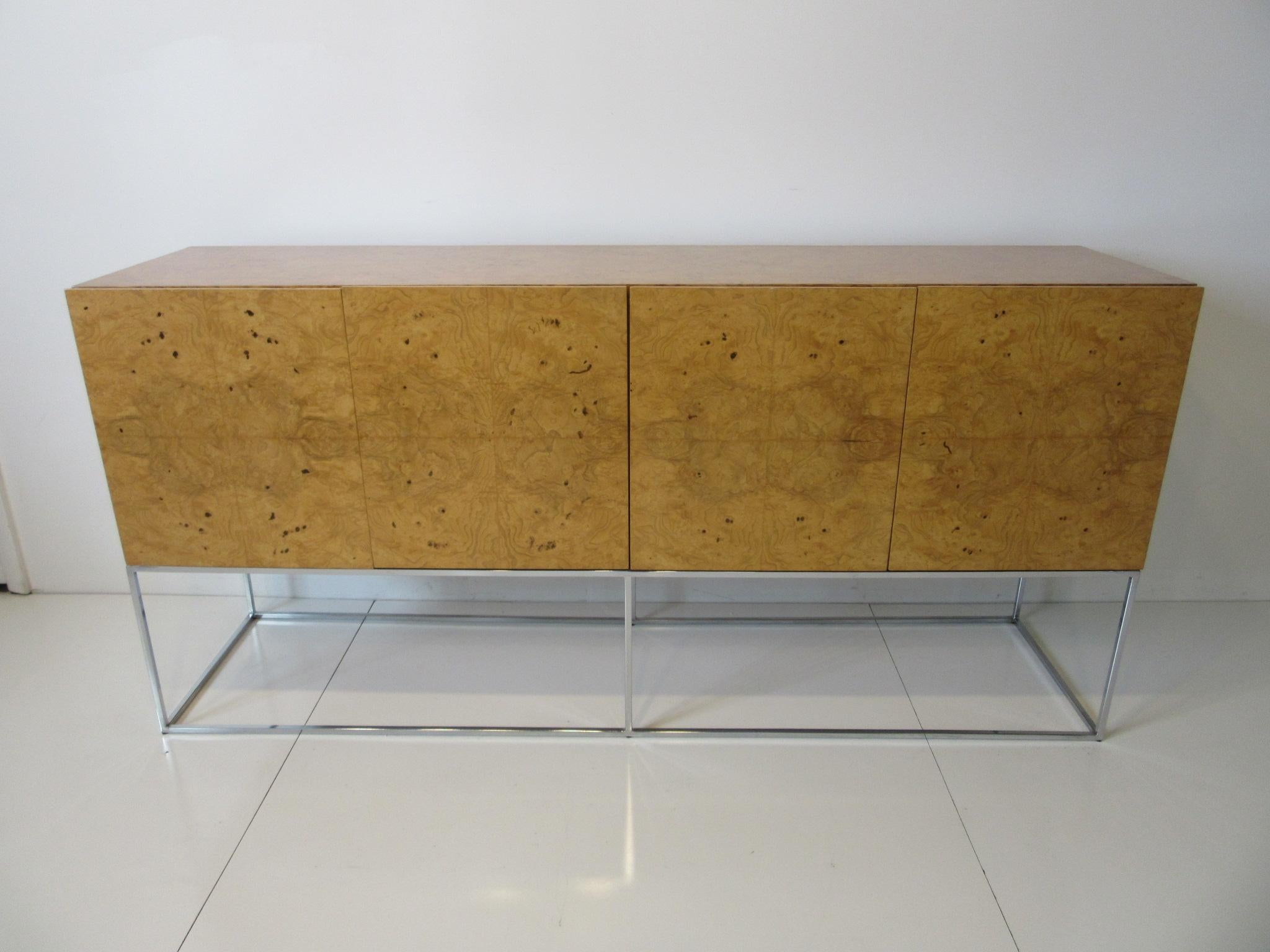 A beautifully book matched four door olive wood burl credenza or server floating on a polished chrome squared tubed steel base having two drawers and storage with two adjustable shelves. By Milo Baughman this is one of his most sought after designs