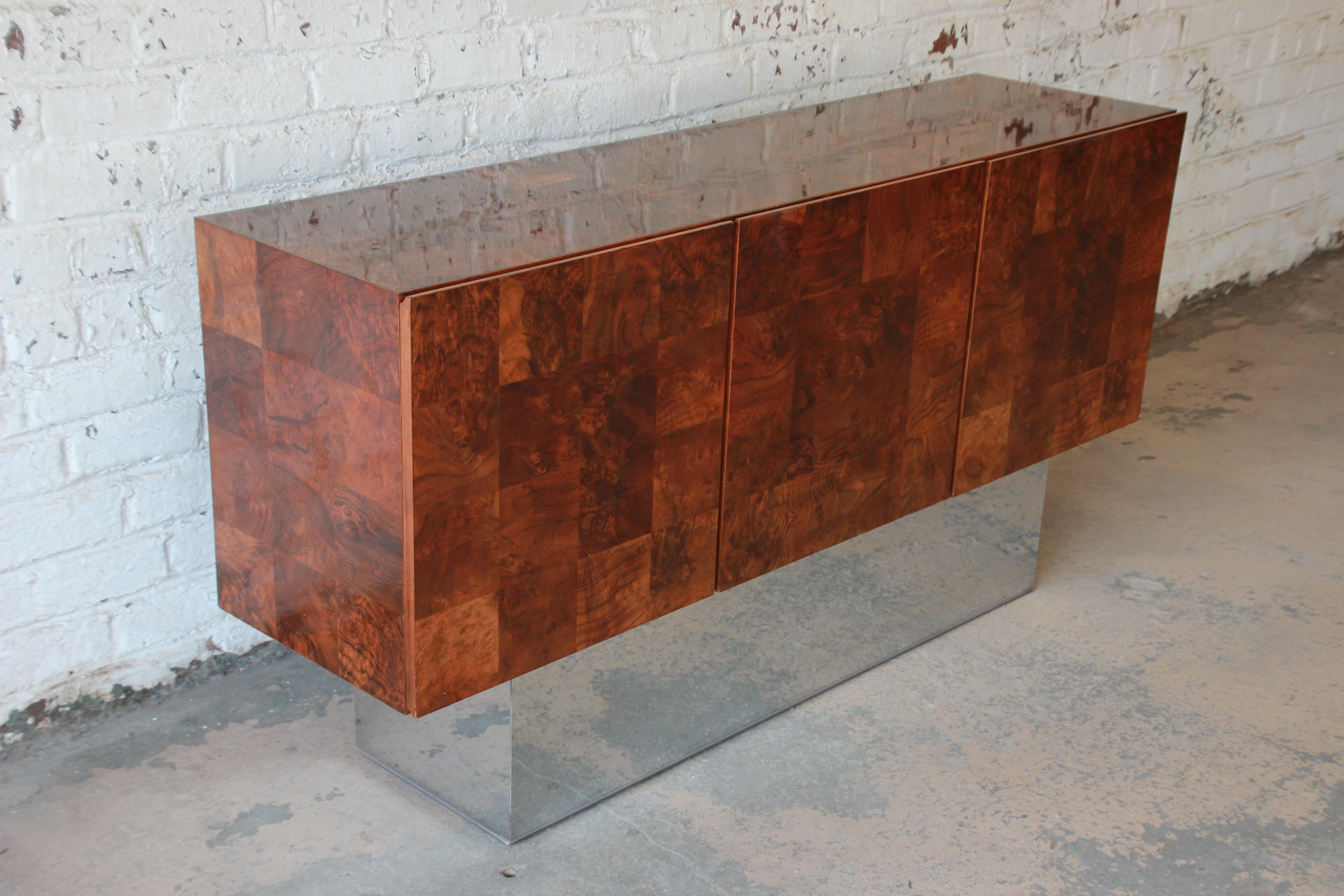 An exceptional Mid-Century Modern patchwork burl wood and chrome sideboard credenza designed by Milo Baughman. The credenza features stunning burled walnut wood grain and a sleek, tall chrome plinth base. It offers ample room for storage, with four
