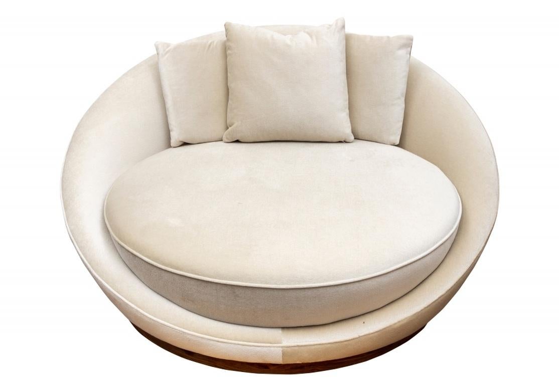 A Classic Modern piece. A large, deep round chair with the seat in one piece with the frame. Upholstered overall in an ecru fabric with three matching toss pillows. Mounted on a circular nicely grained wood base.
Depth 55
