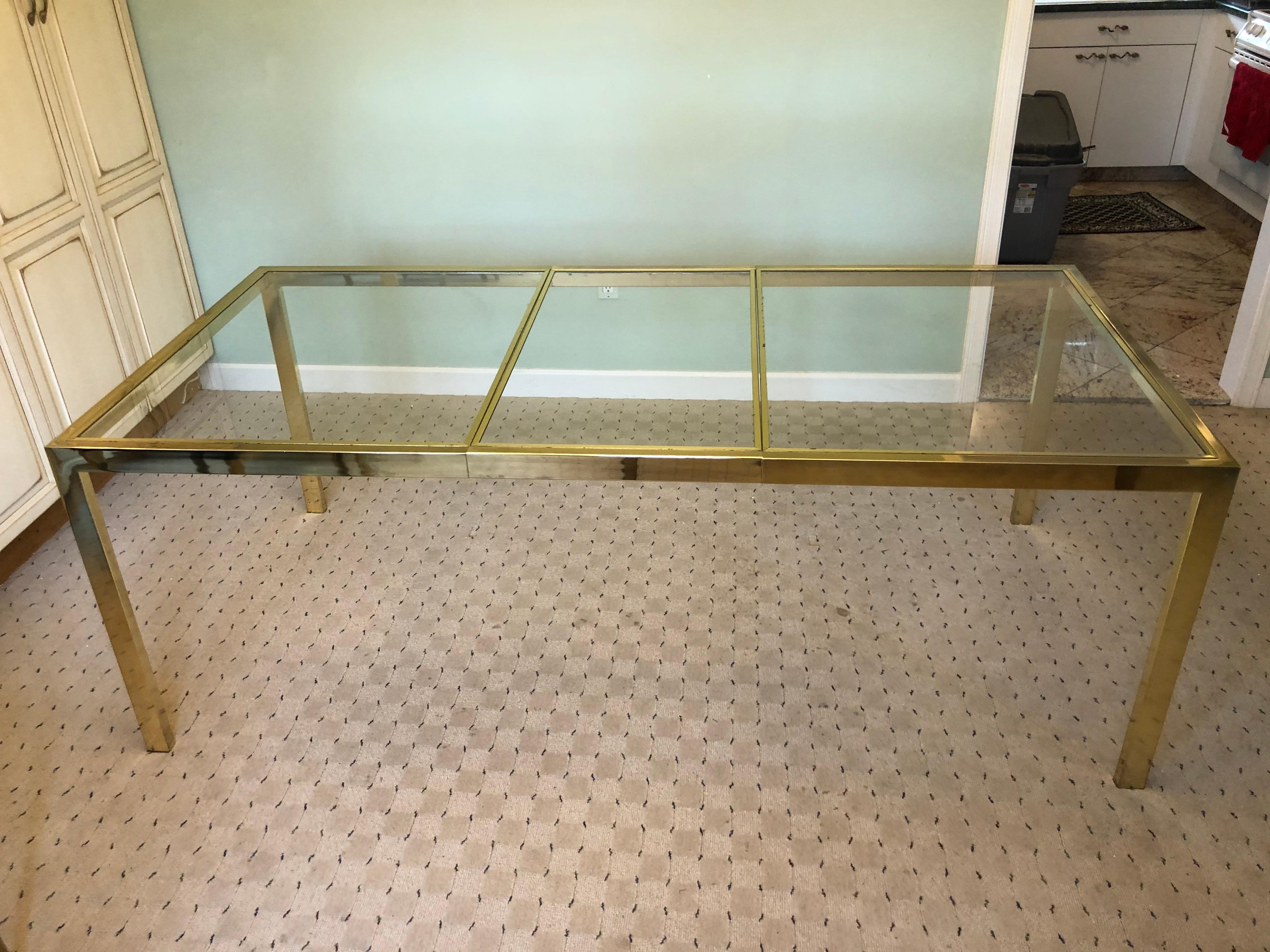 Milo Baughman style adjustable brass dining table.
The glass top separates into three glass panels that lift out and the table then can shrink to be smaller on its own track.