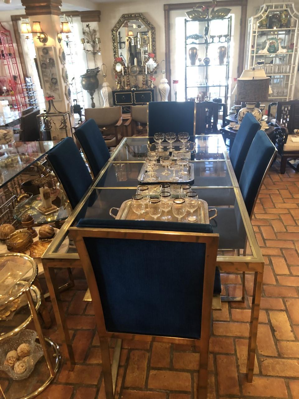 Milo Baughman style adjustable brass dining table set.
The glass top separates into three glass panels that lift out and the table then can shrink to be smaller on its own track. Set of 6 brass dining chairs in blue velveteen. Two armchairs that