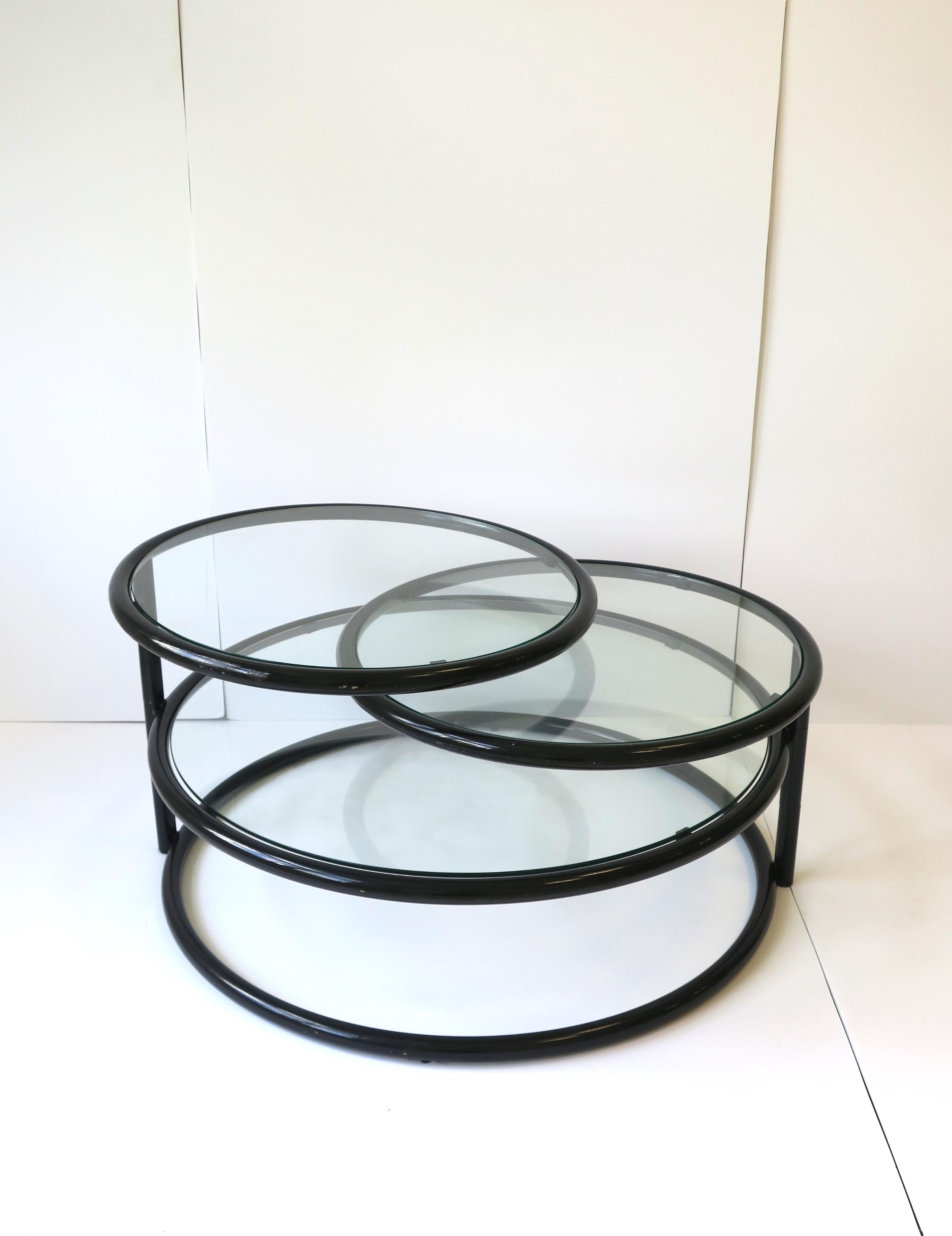 A Modern style Postmodern period three tier black coated tubular metal and glass swivel cocktail table in the style of designer Milo Baughman, circa late-20th century, 1970s or later. The top two tiers of this versatile cocktail table swivel out as