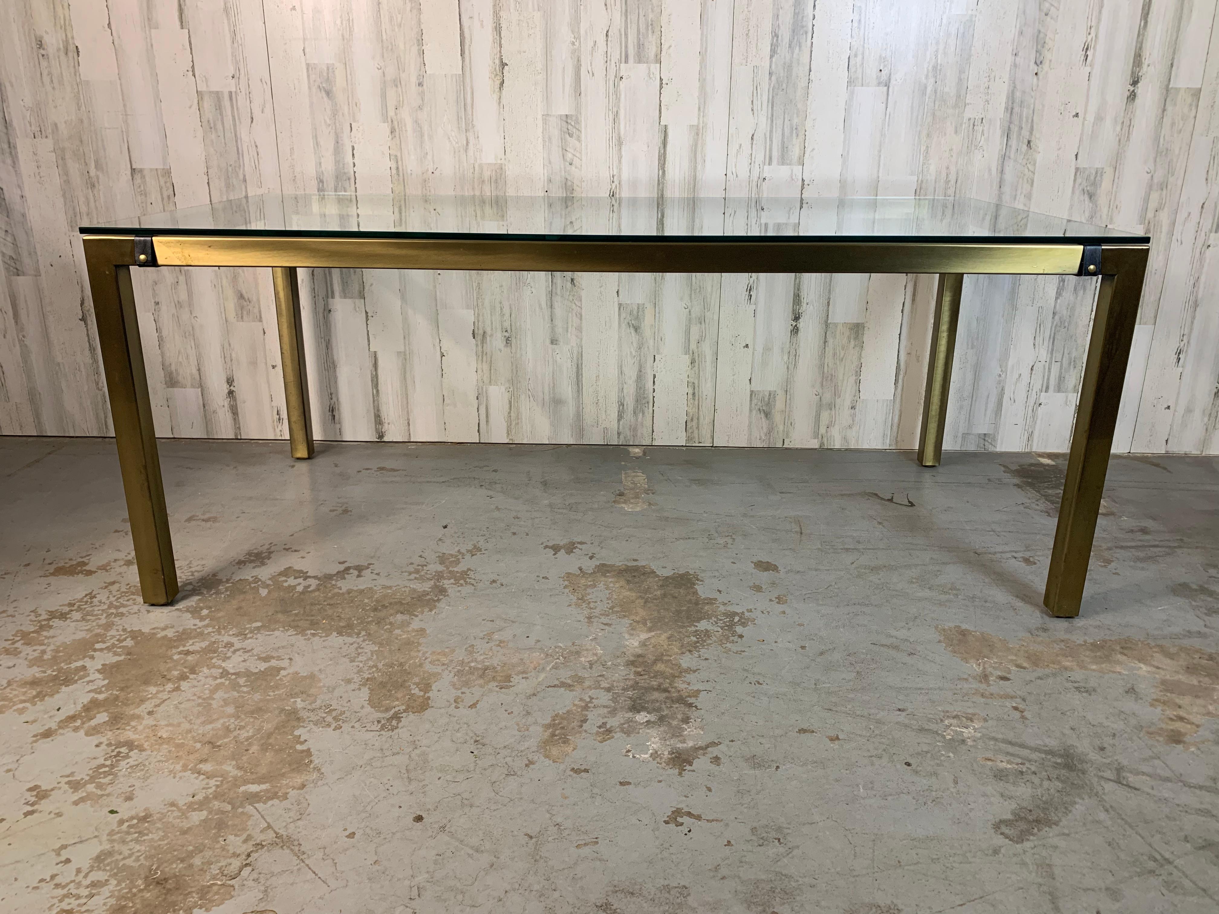 Nice vintage patina on the brass finish with faux leather snap straps that make the glass top appear floating. Parsons style table can go with any style chairs from antique to modern .