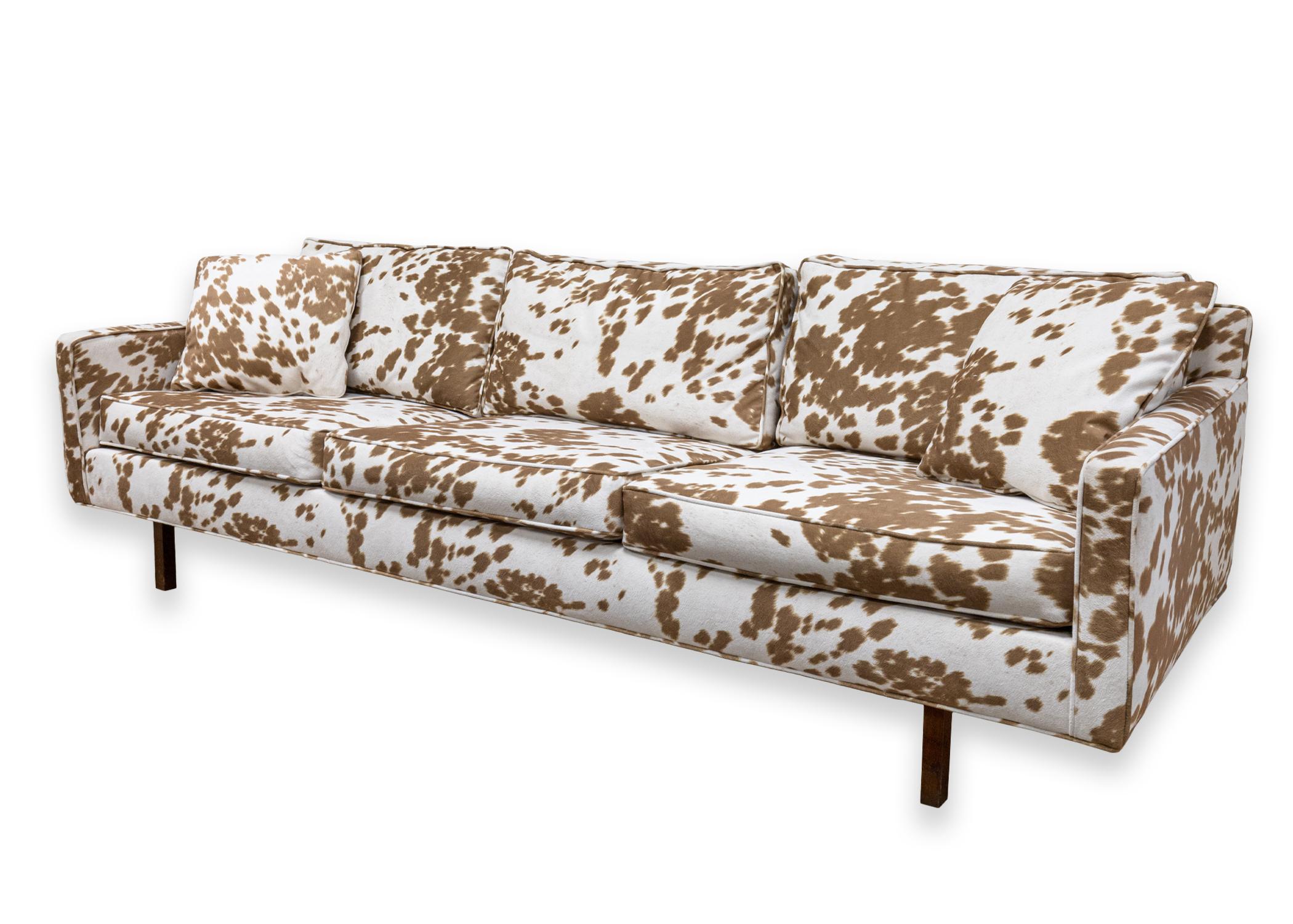 A Milo Baughman Style Directional sofa. A wonderful sofa featuring a super unique brown and white cow print upholstery. This sofa features removable cushions, two matching throw pillows, and exposed wooden legs. This sofa is in very good condition.