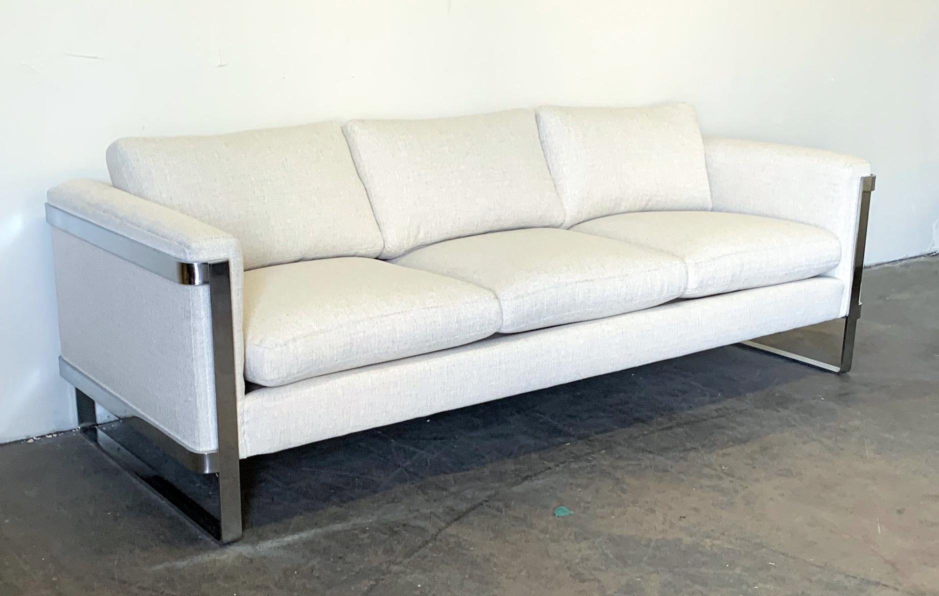 Often attributed to Milo Baughman, this stunning sofa features chrome flat bar sides that wrap the sides of the sofa. This stunning sofa is both masculine and chic all at the same time. This sofa features clean lines, and an off-white light oatmeal